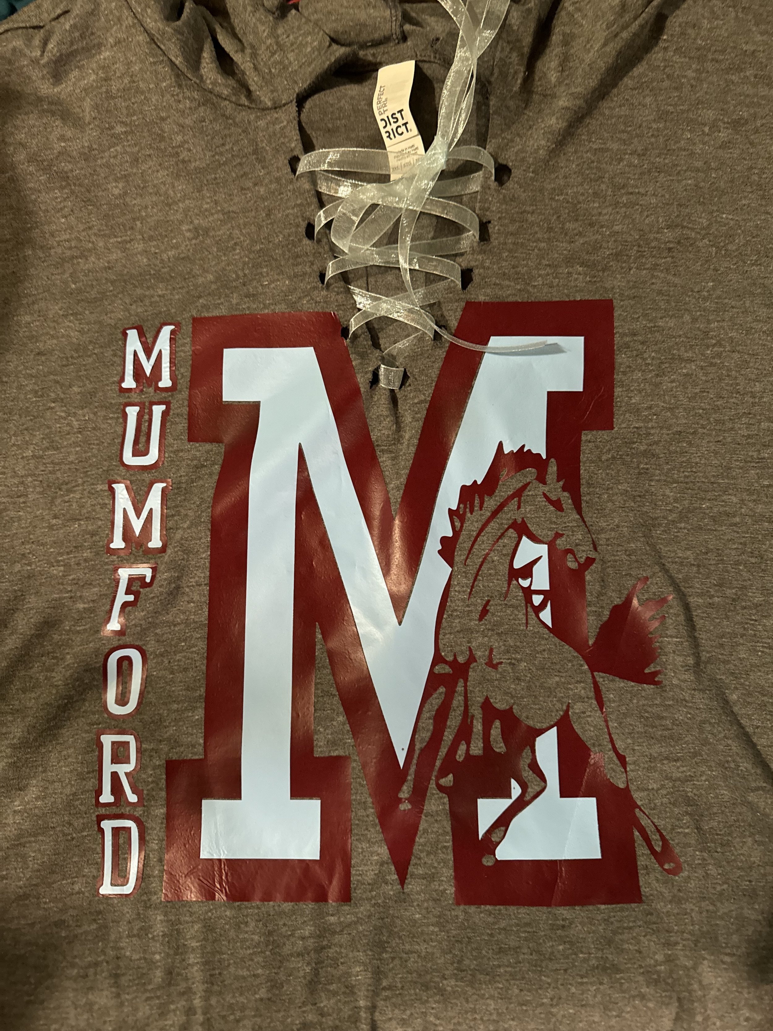 A brown T-shirt with a large letter 'M' and a cartoon horse mascot for Missouri University of Missouri on it, with the word 'MUMFORD' listed vertically on the left side.