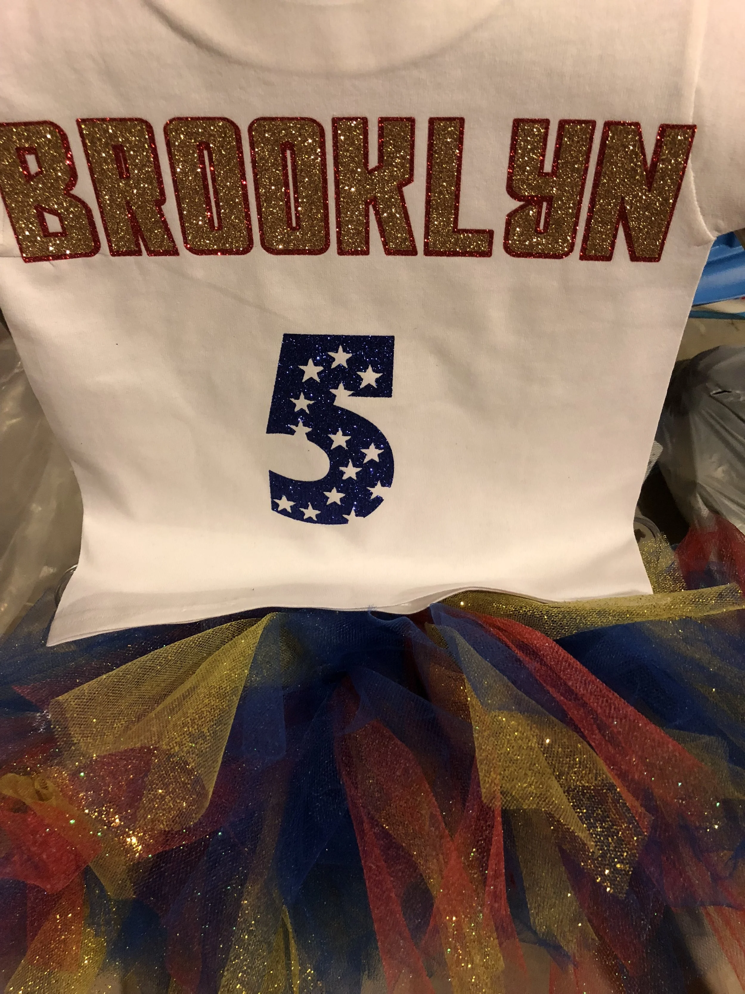 Decorative shirt with the name 'Brooklyn' in glittery red and gold text, the number '5' with star pattern, and colorful tulle fabric underneath.