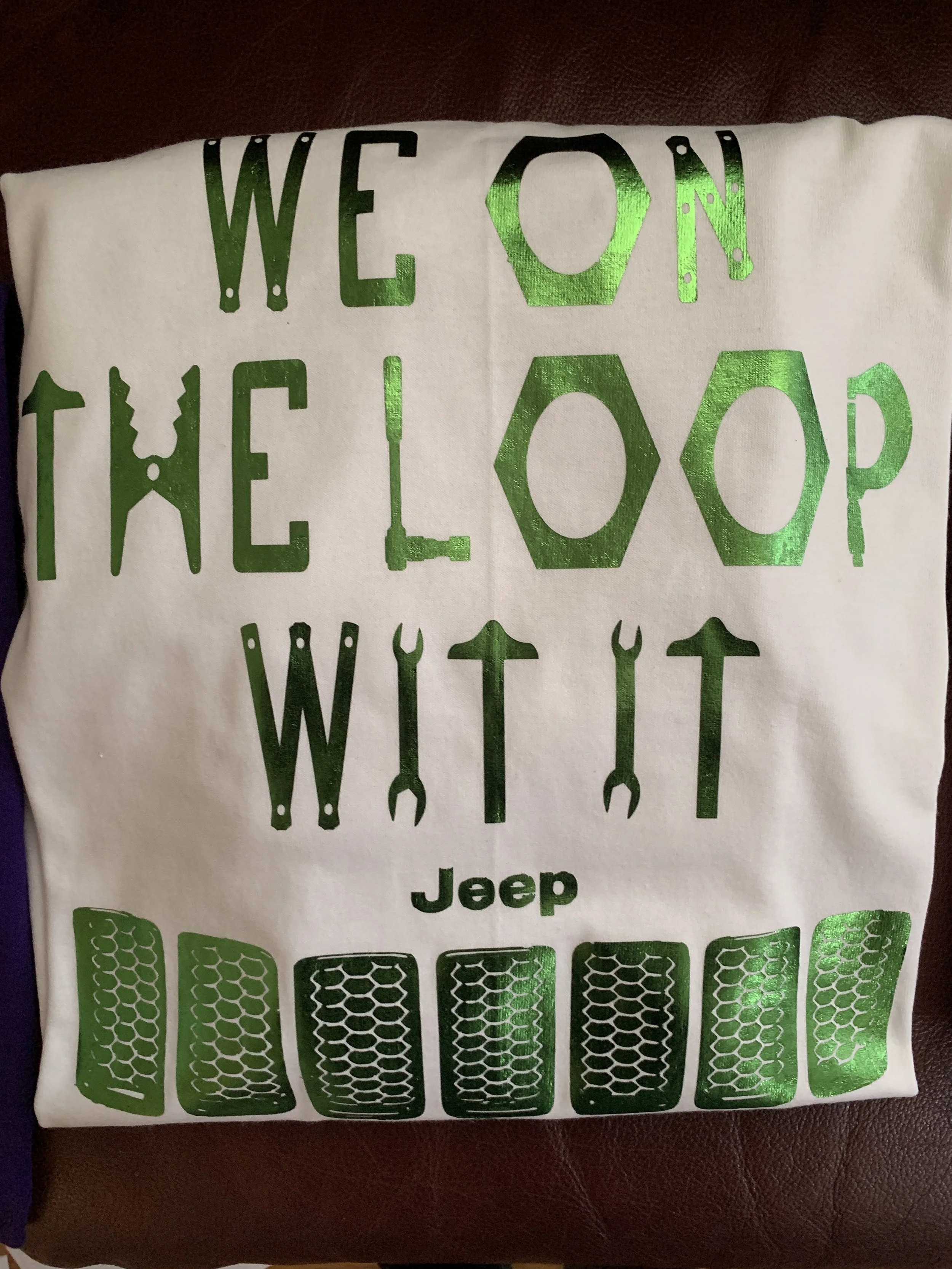 White fabric with green metallic and black print that reads "We ❤ on the loo, the loo, wit it" and has illustrations of wrenches and tire treads, with the Jeep logo in the center.