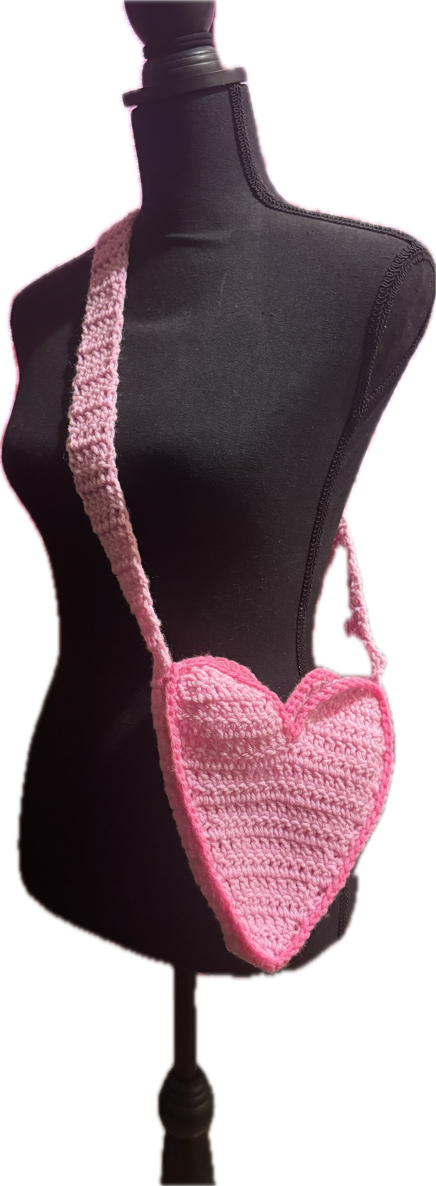 A black dress form mannequin with a pink crocheted heart-shaped purse hanging on its side.