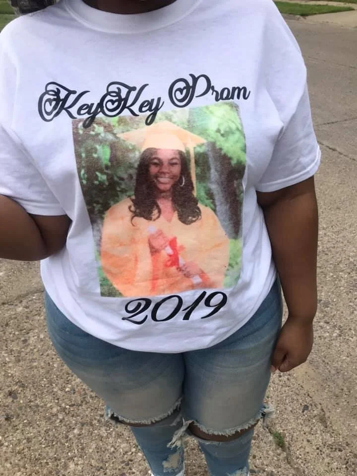 A woman wearing a white T-shirt with a photo of a young girl holding a diploma, and the words 'Key Key Prom 2019' above and below the photo.