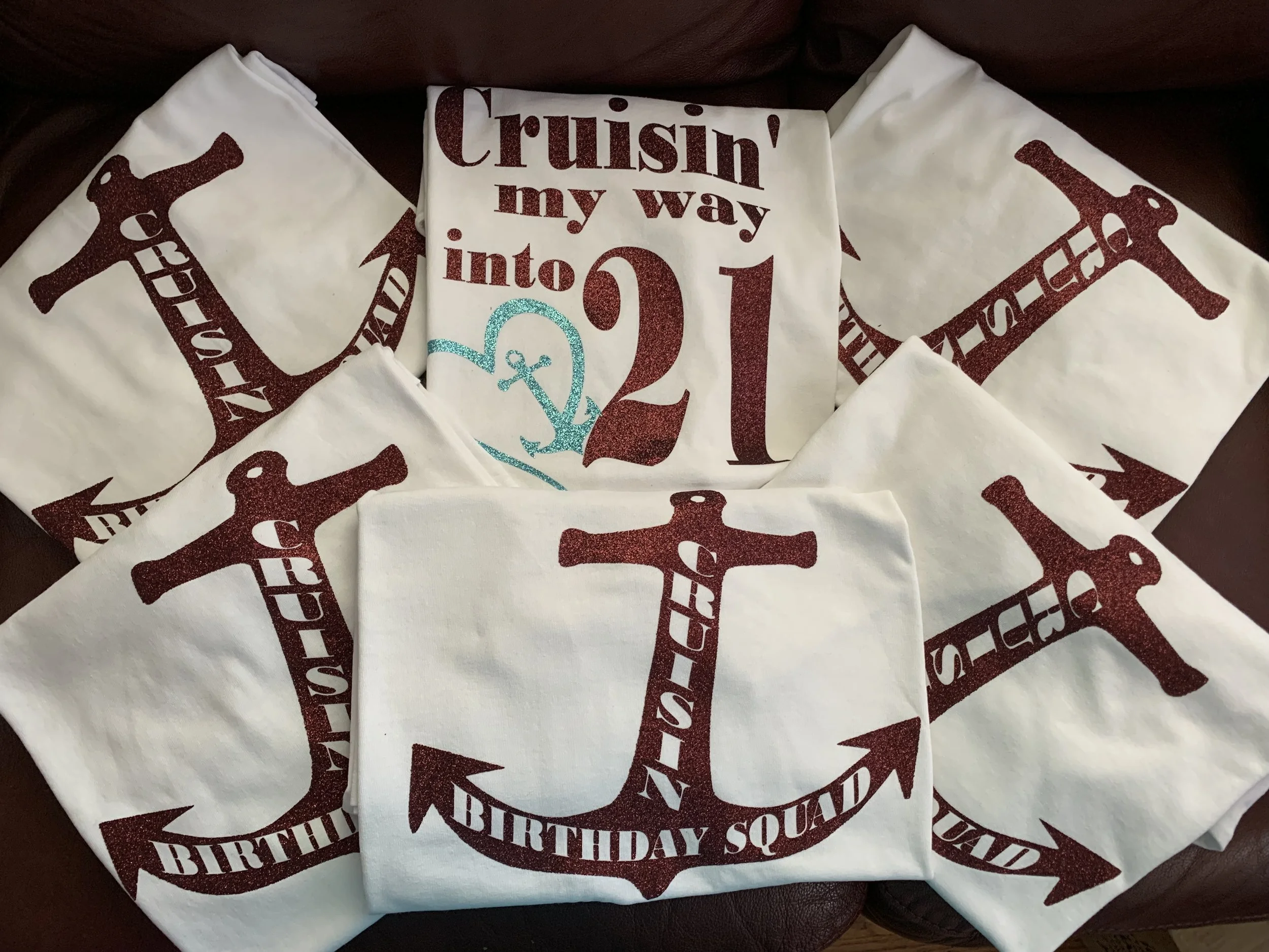 A centerpiece with a birthday shirt and several white napkins featuring an dark red anchor design and the words "BIRTHDAY SQUAD" around the anchor. The shirt has the phrase "Cruisin' my way into 21" with a blue anchor illustration.