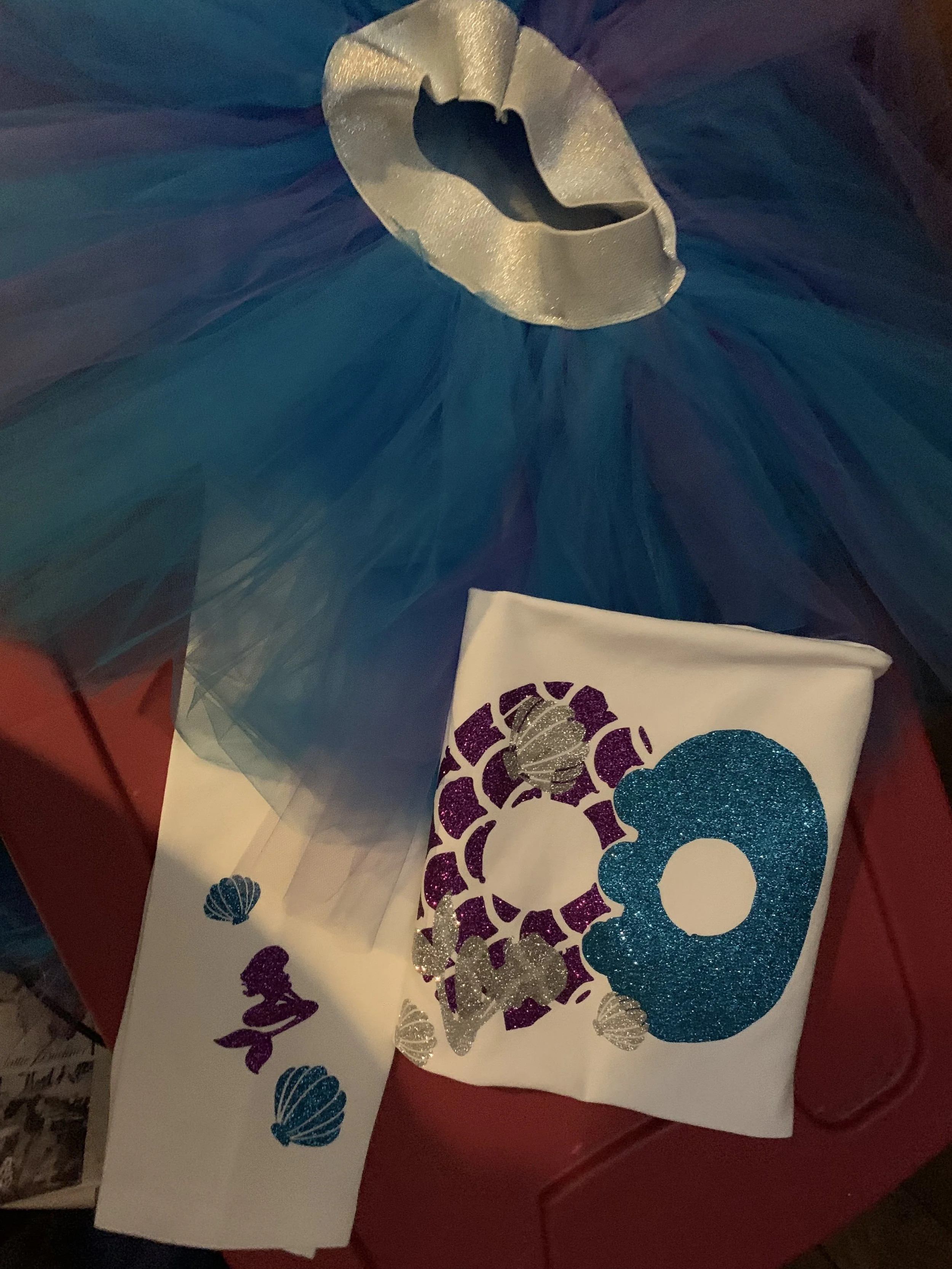 A diaper with a glittery purple seashell, a glittery blue number 8, and smaller seashells. Tulle fabric with a silver ribbon on top.