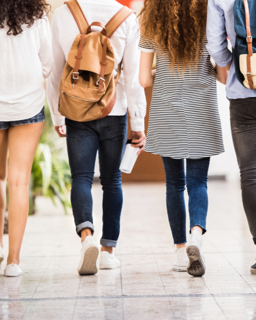 Group of four people walking indoors, two are carrying backpacks and one is holding a water bottle.