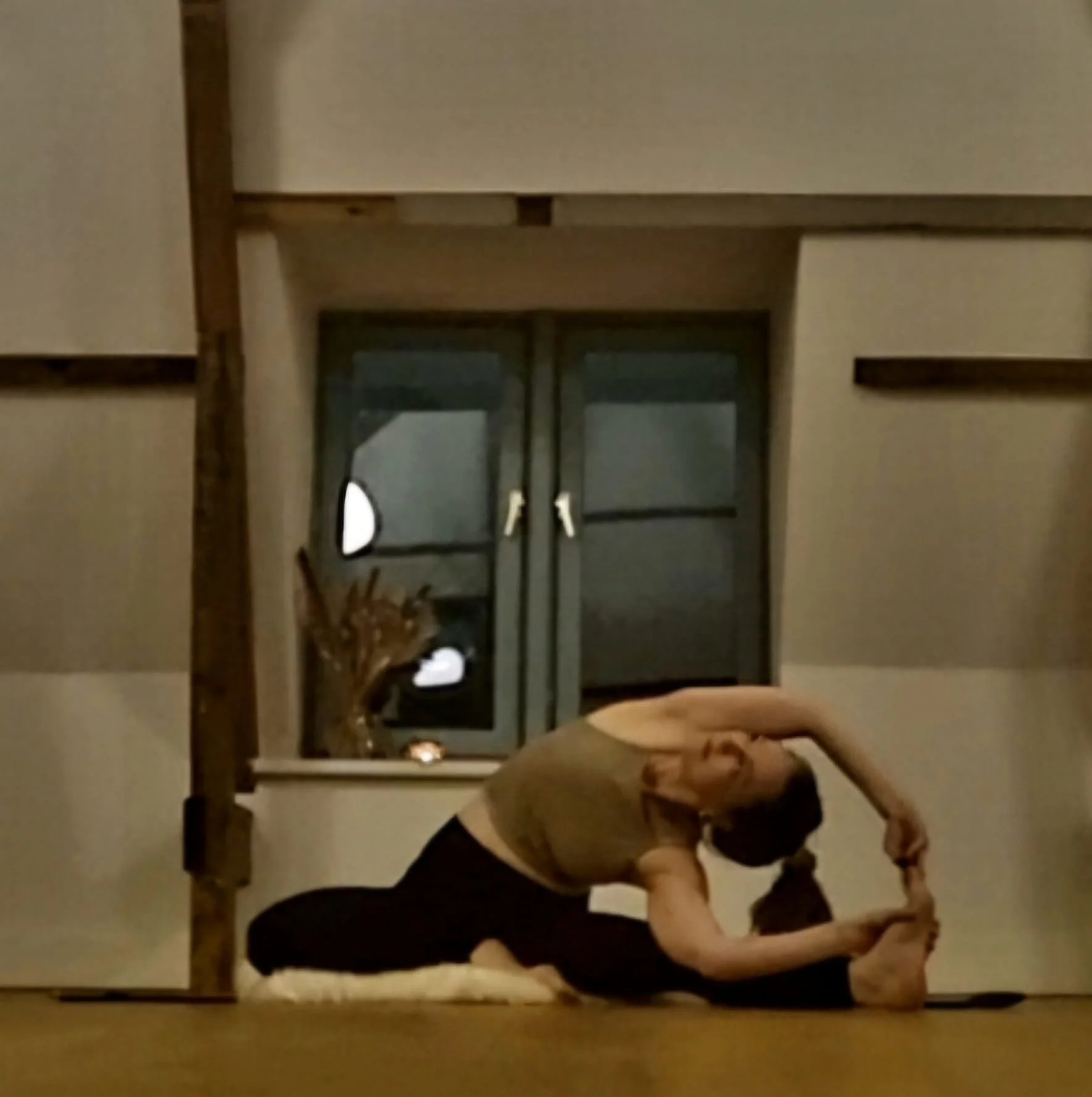A woman practicing yoga in a room, sitting on a yoga mat in a seated forward bend pose with her arms extended over her head, reaching for her feet. In Diemen.