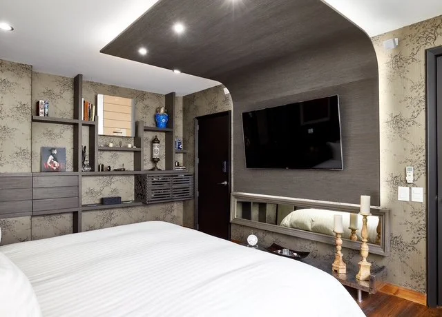 Modern bedroom with decorated wall shelves, a wall-mounted TV, a mirror, and a bed with white linens.