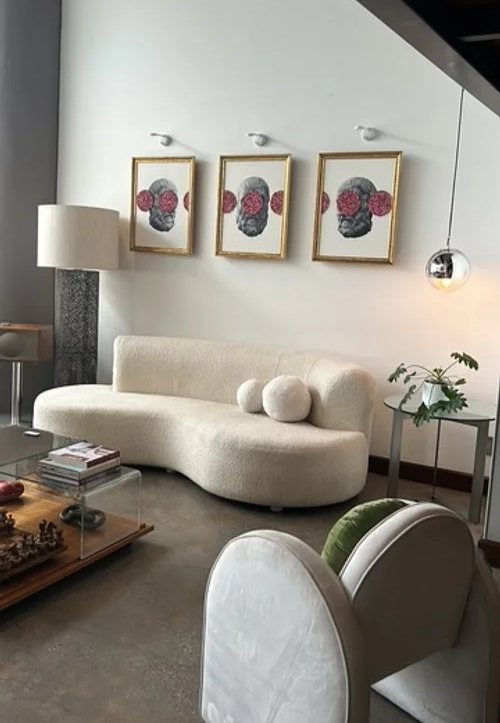Modern living room with a white curved sofa, a glass coffee table, and framed art of a skull with pink flowers on the wall.