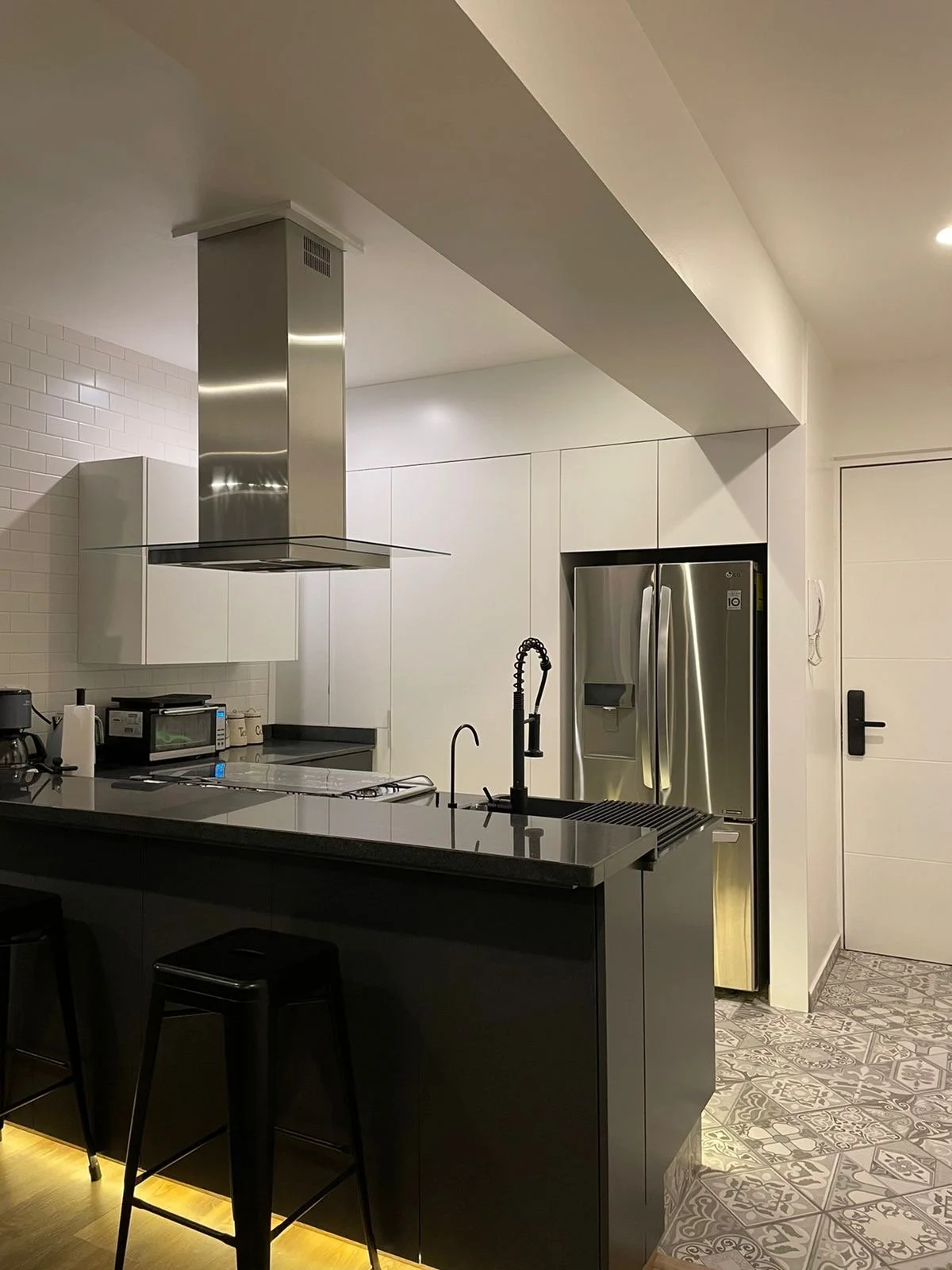 Modern kitchen with a black island, stainless steel refrigerator, black bar stools, and patterned tile flooring.