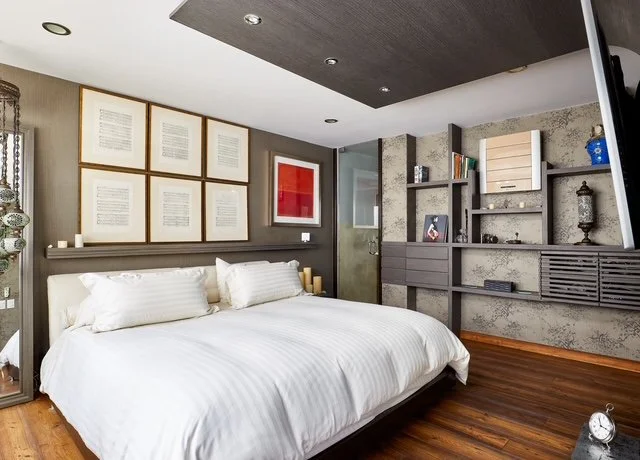 Modern bedroom with a white bed, framed artwork above, and gray shelving with decorative items.