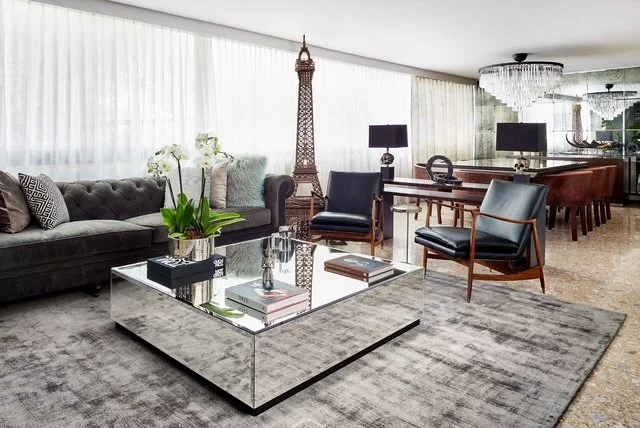 Modern living room with black sofa, armchairs, glass coffee table, and decorative Eiffel Tower statue.