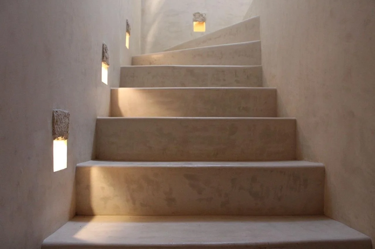 Wooden staircase with small square cutouts in the wall allowing light to shine through.