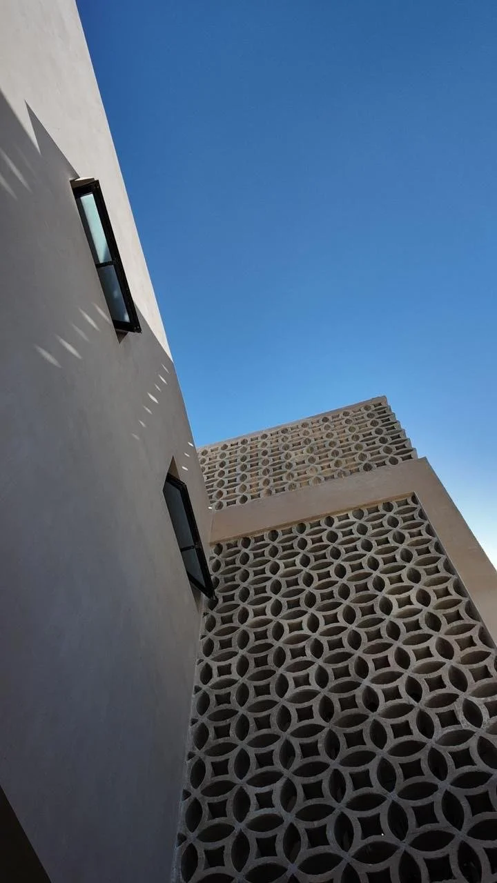 View of modern building with decorative patterned wall panels and two small windows, against a clear blue sky.