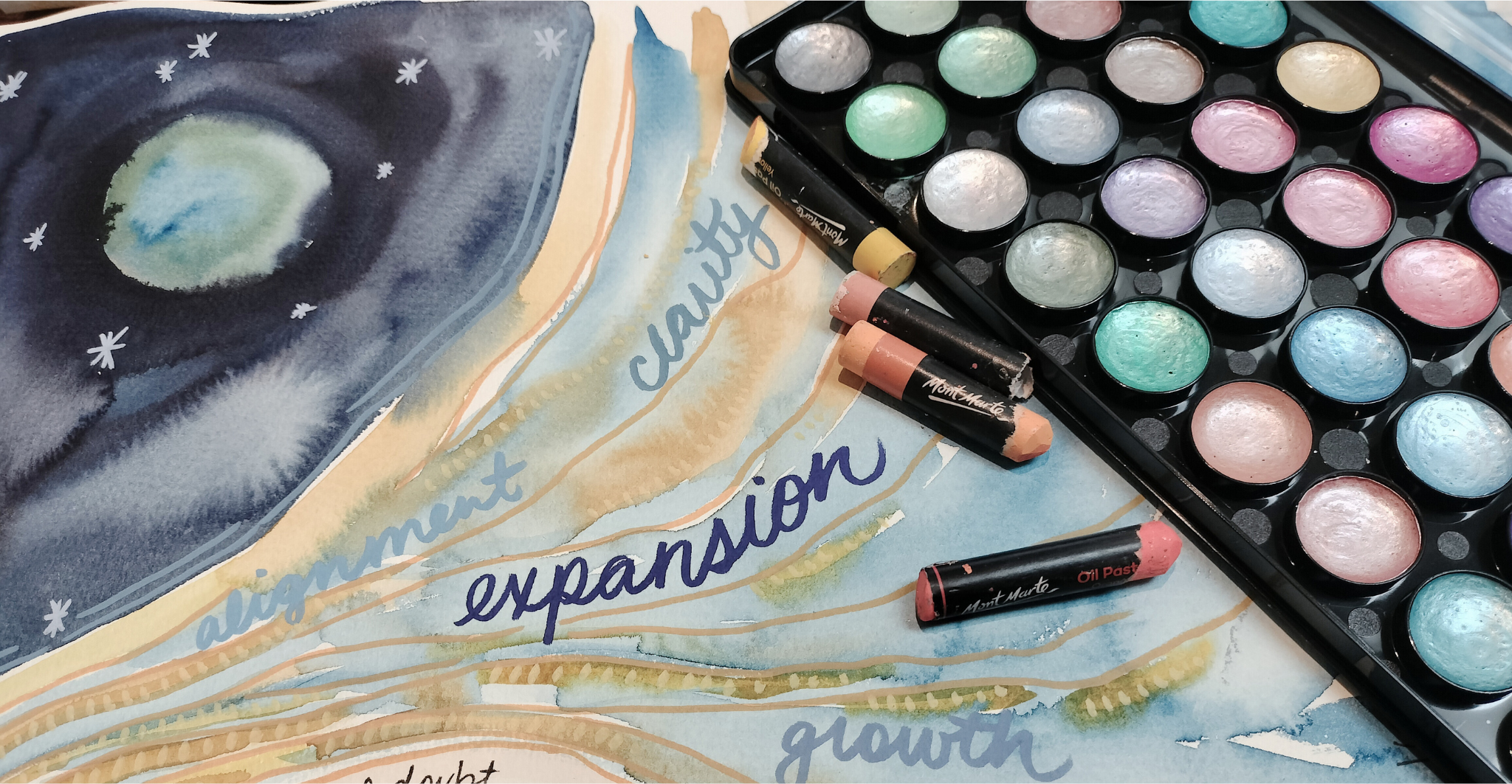 Watercolor painting with words like 'alignment,' 'clarity,' 'expansion,' 'growth,' and 'thought,' along with a palette of pastel watercolor paints and pastel sticks.