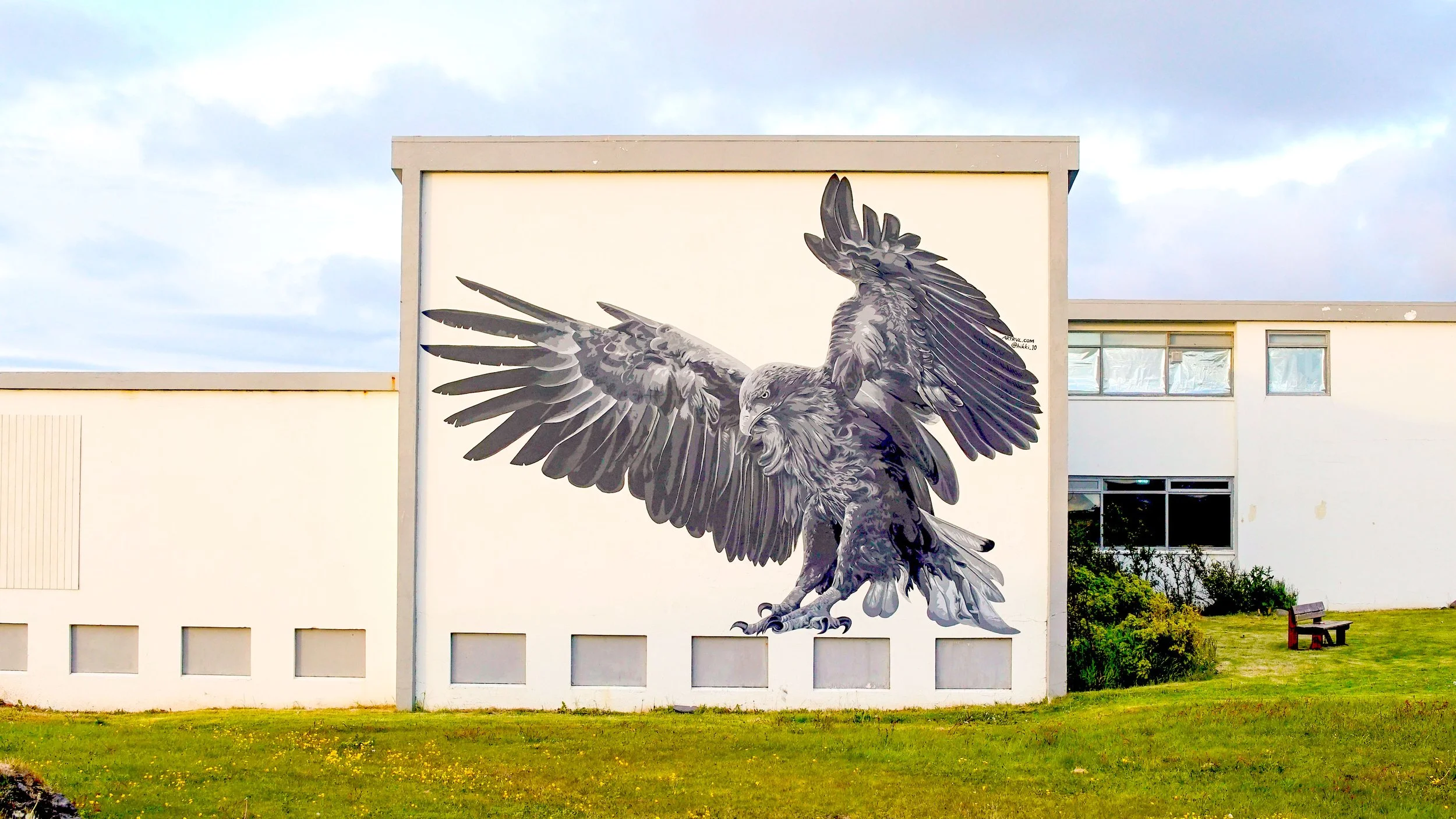 A large mural of an eagle with outstretched wings is painted on the side of a building, outdoors with a grassy area in front.