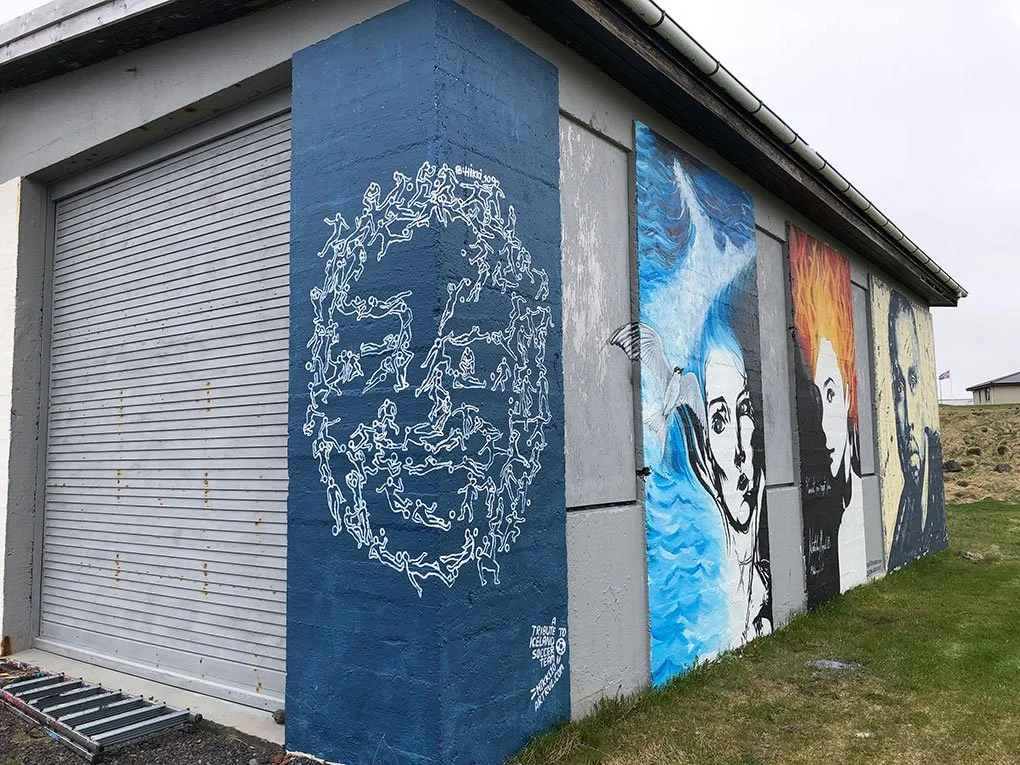 Street art mural featuring stylized portraits of women and a large face composed of running figures on a building wall.