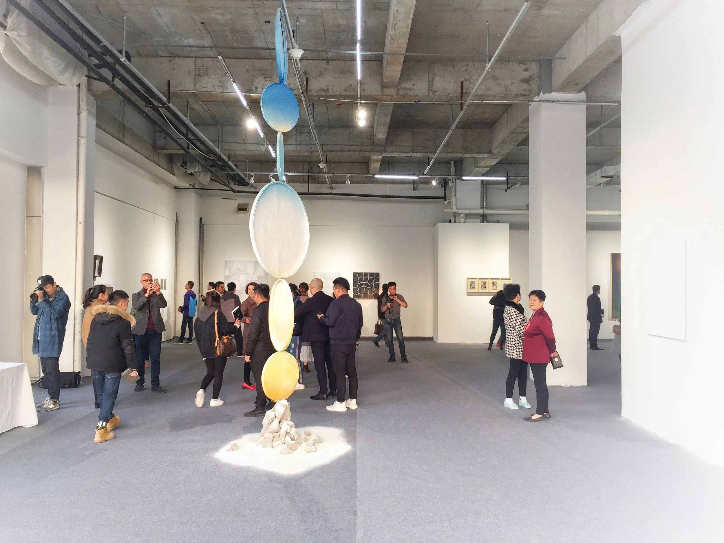 People viewing art exhibit in a gallery with sculpture hanging from the ceiling