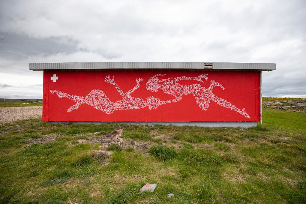 A red building with a white outline of a dragon on the side, positioned on grass with a cloudy sky in the background.
