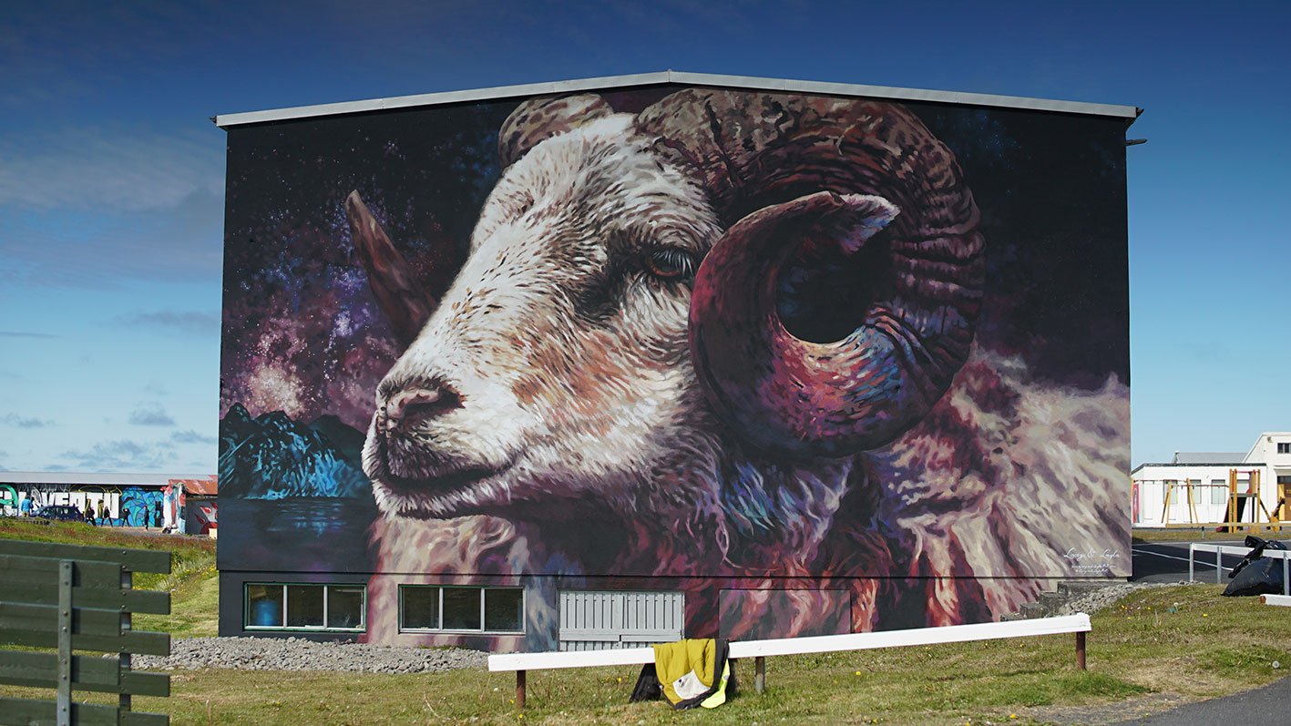 Large mural of a goat's head with intricate details, set against a cosmic background with stars and nebulae, on a building exterior.