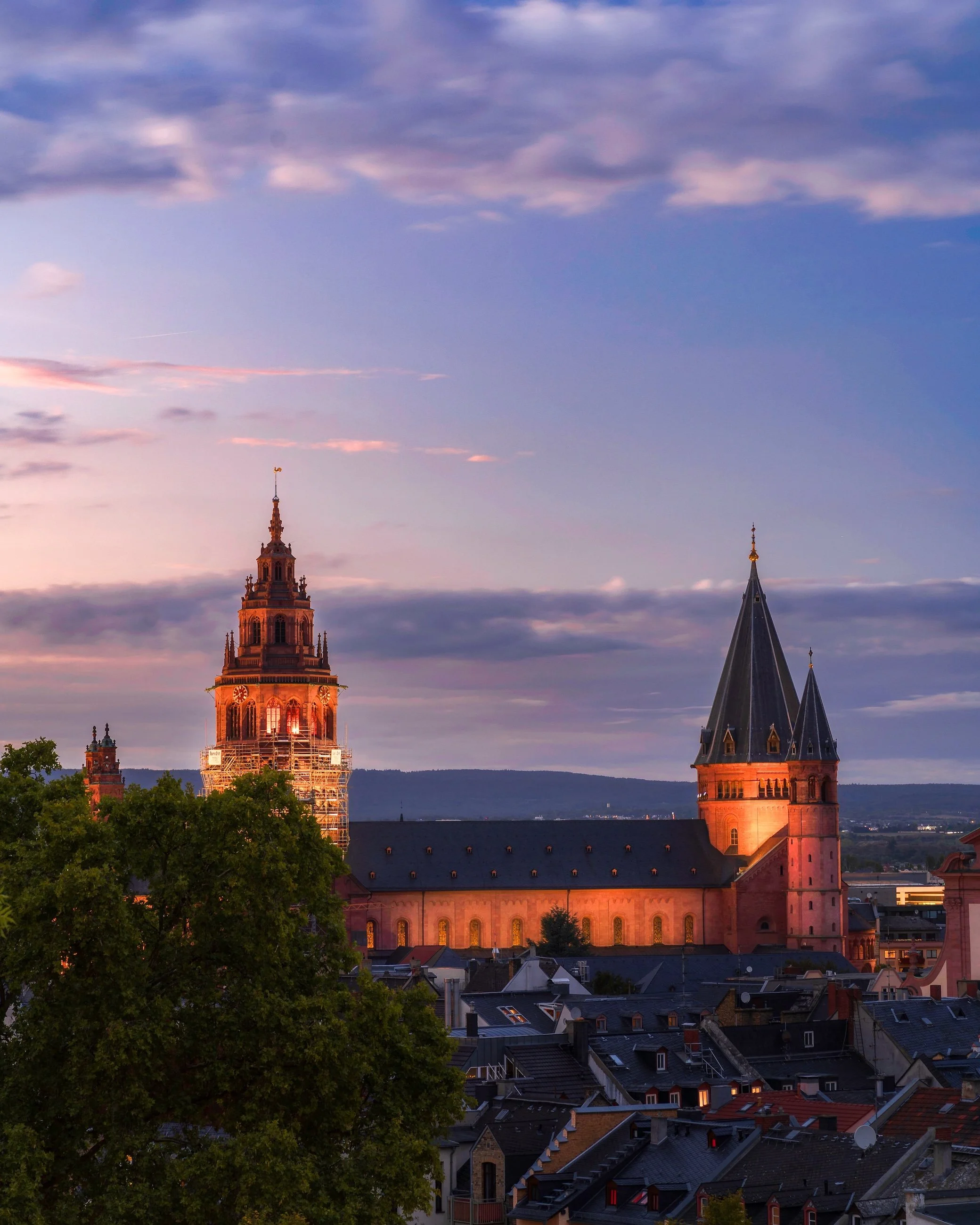 Eine Stadtansicht bei Sonnenuntergang mit historischen Gebäuden, zwei Kirchtürme, und einem bewölkten Himmel.