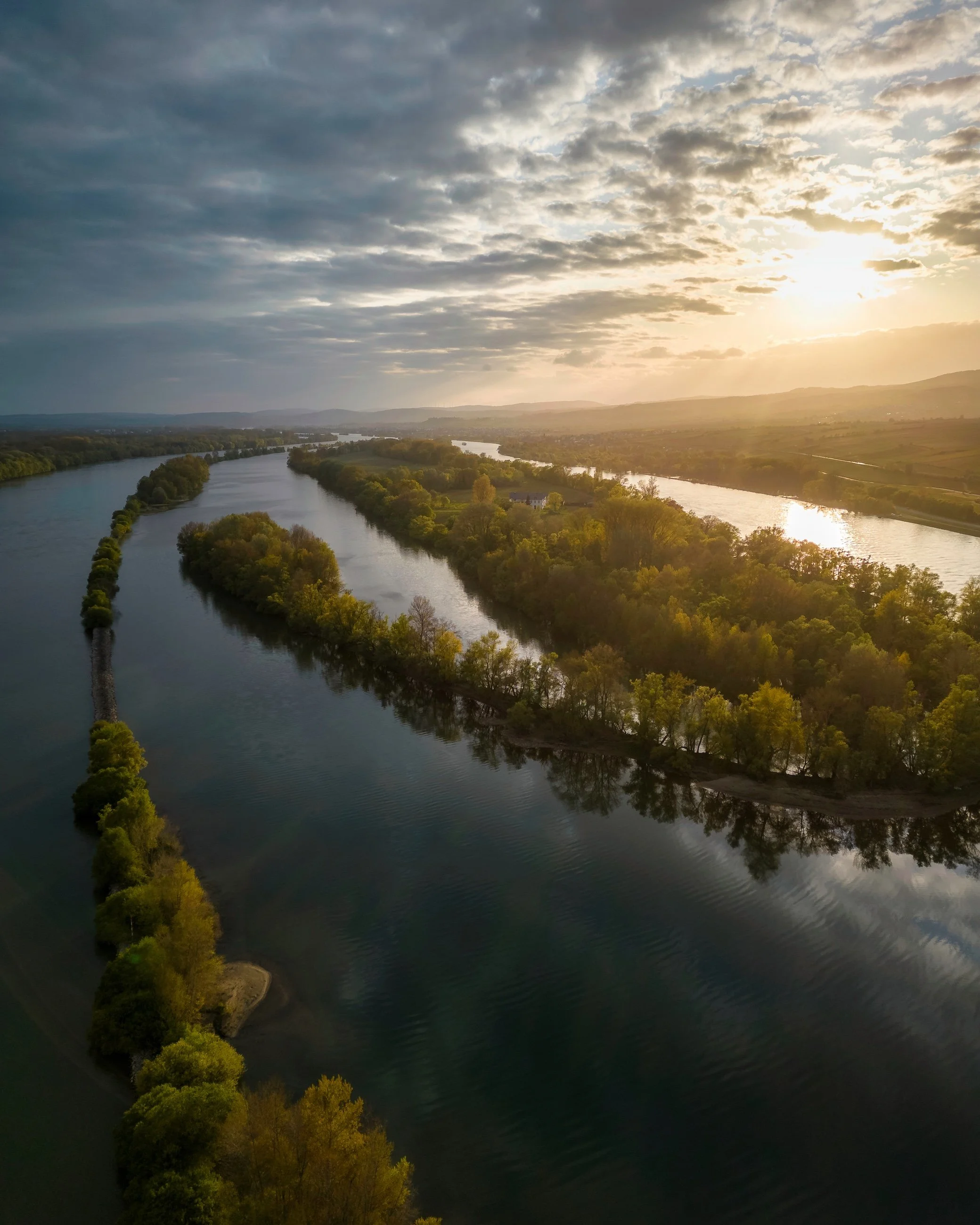 Ein Fluss mit umgebenen Bäumen bei Sonnenuntergang, bewölkter Himmel