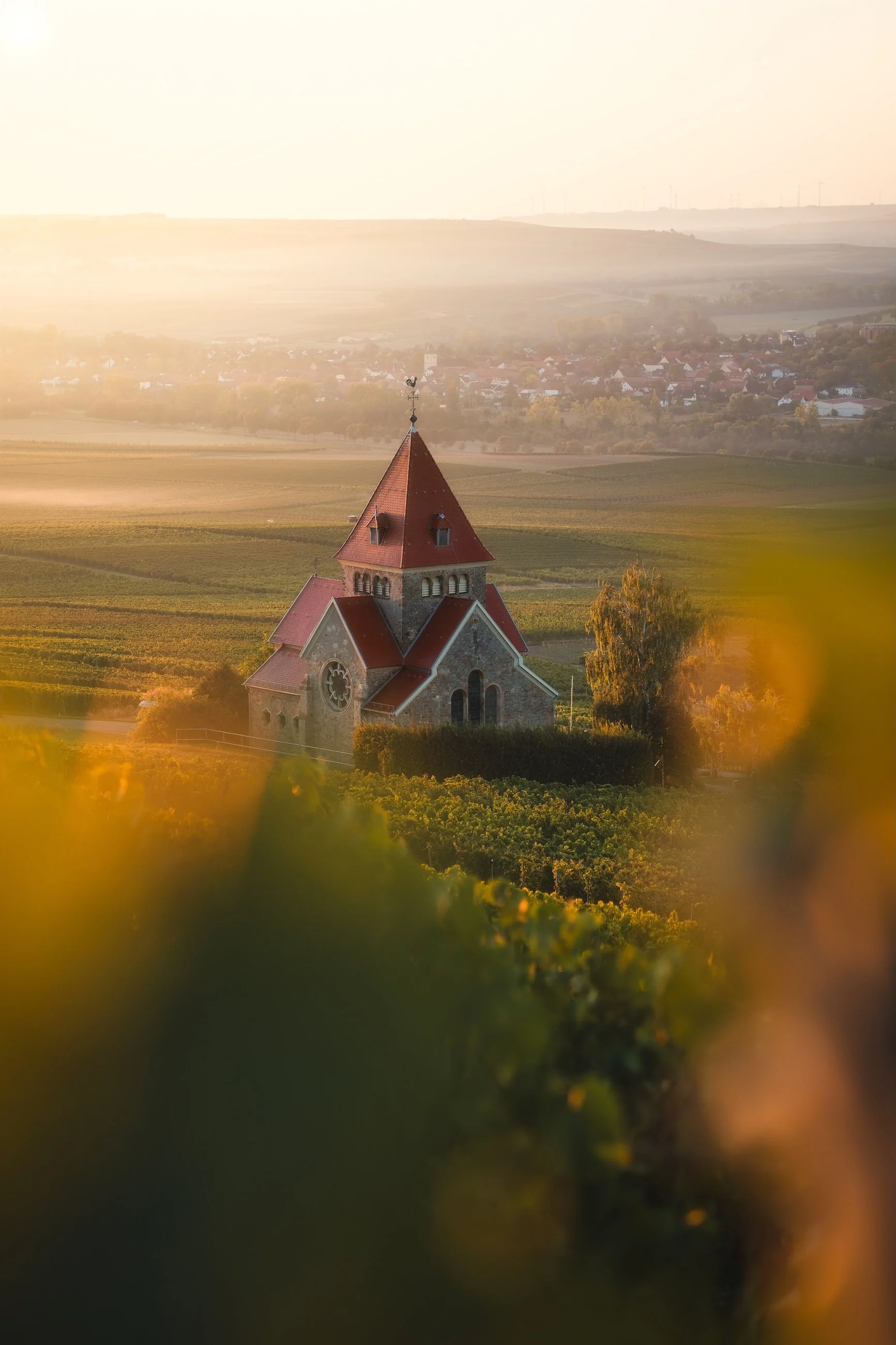 Ein mittelalterliches Kirchgebäude mit roten Dächern inmitten einer ländlichen Landschaft bei Sonnenuntergang.