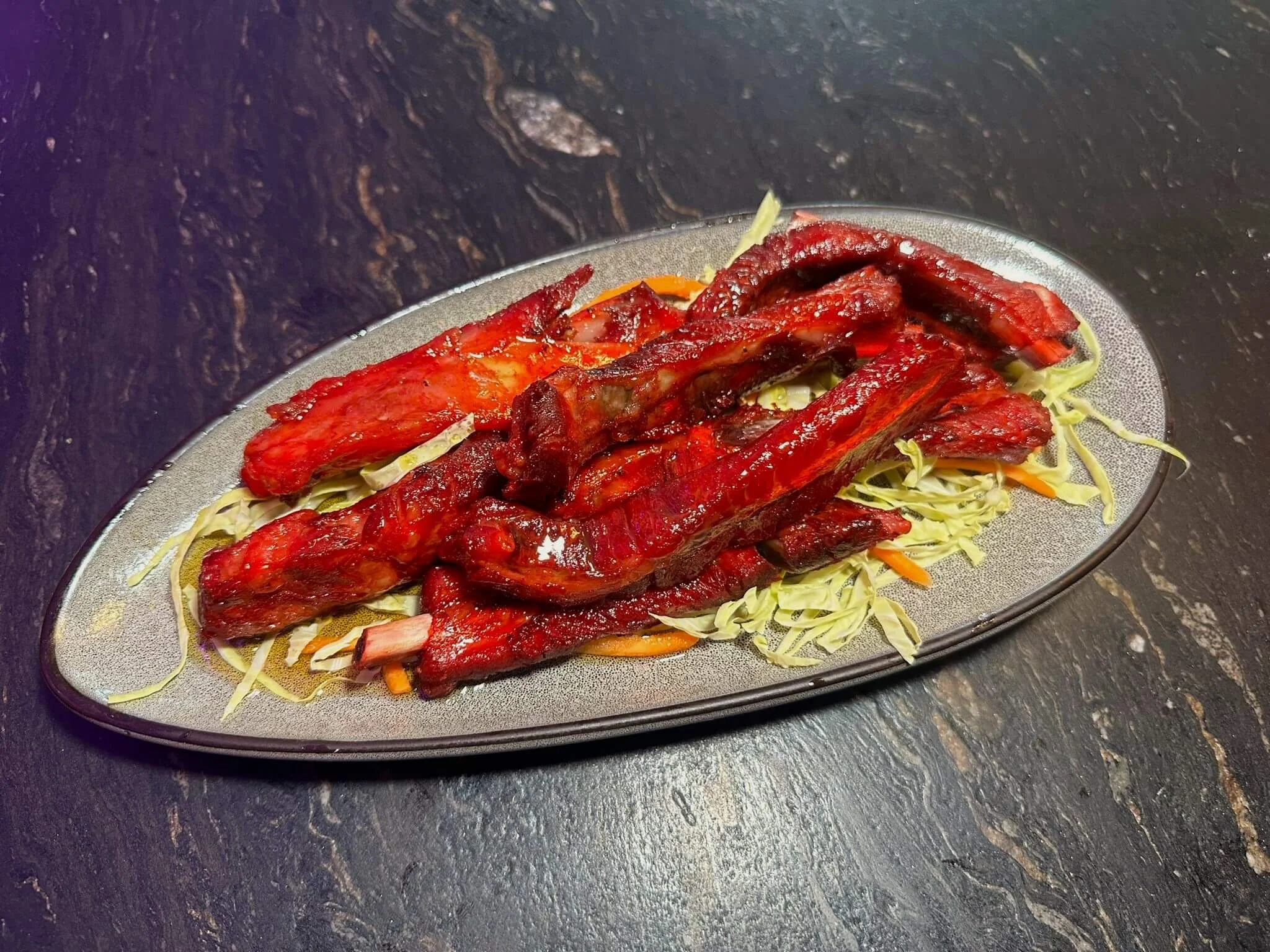 Barbecue pork ribs served on a bed of shredded cabbage and carrots on a silver platter