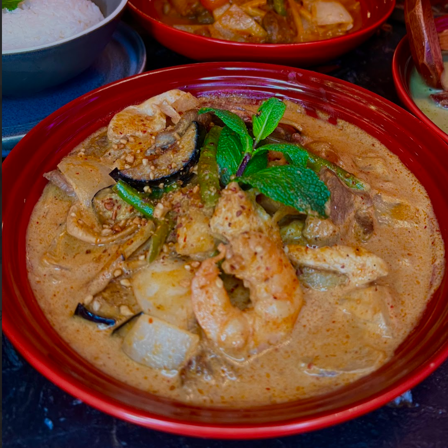 A bowl of Thai red curry with shrimp, eggplant, green beans, topped with fresh mint leaves.