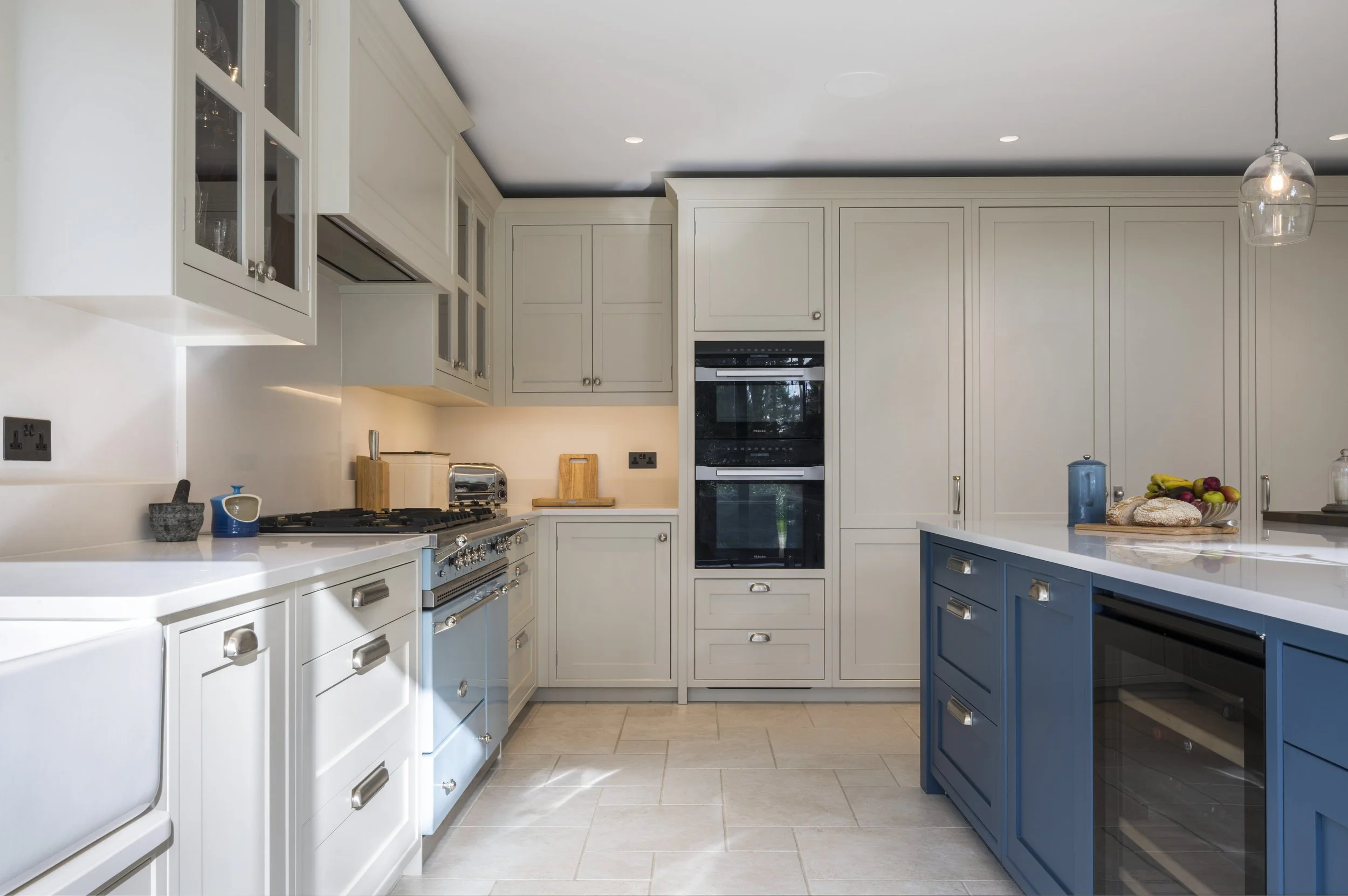 Modern kitchen with white cabinetry, blue island, stainless steel appliances, and a pendant light fixture.