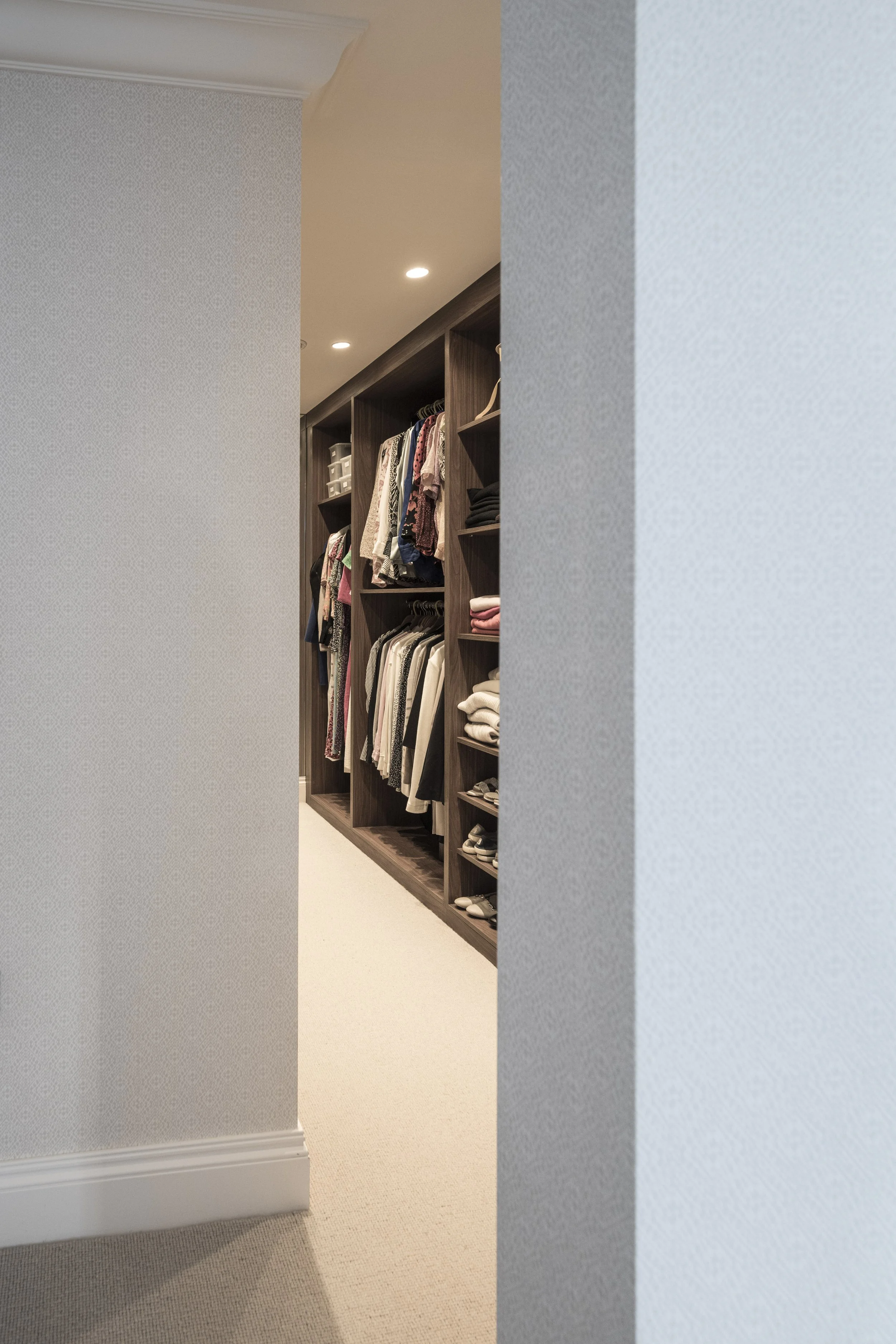 View of an open walk-in closet with shelves and hanging clothes visible, seen through a doorway with partial walls on either side.