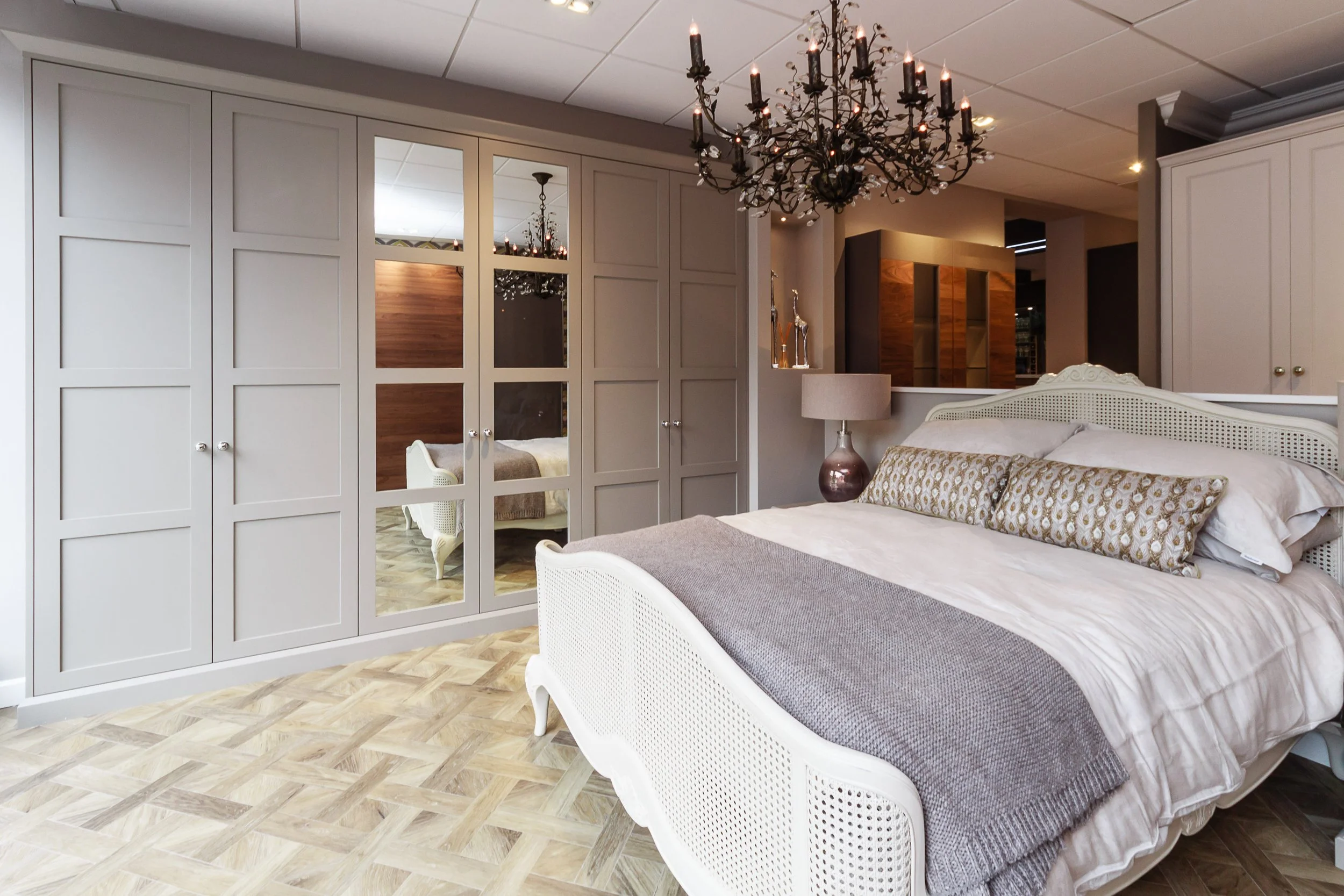 Elegant bedroom with white antique-style bed, patterned pillows, wooden parquet flooring, large wardrobe with mirrored doors, and a chandelier hanging from the ceiling.