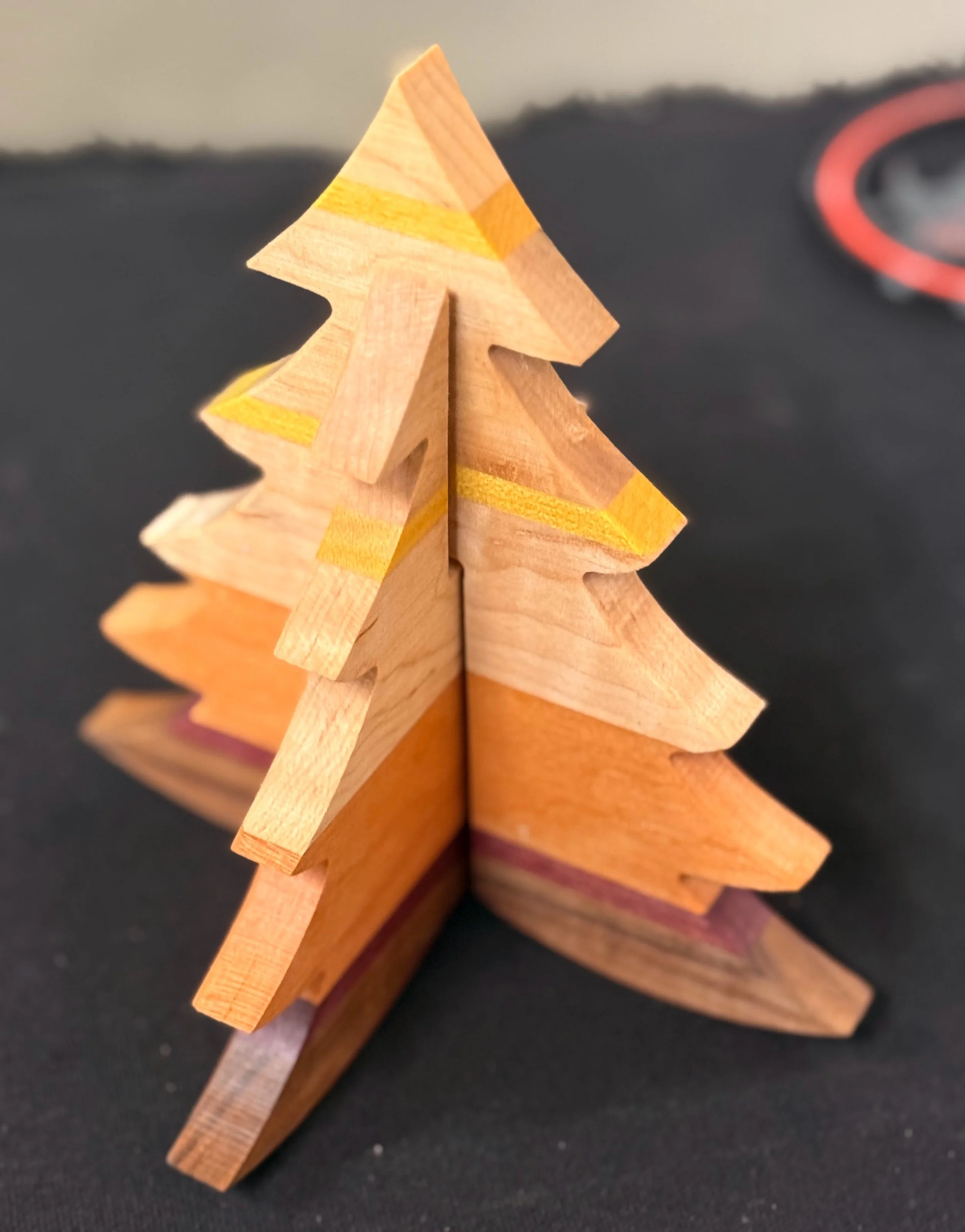 Small wooden Christmas tree with yellow painted accents on a black surface.