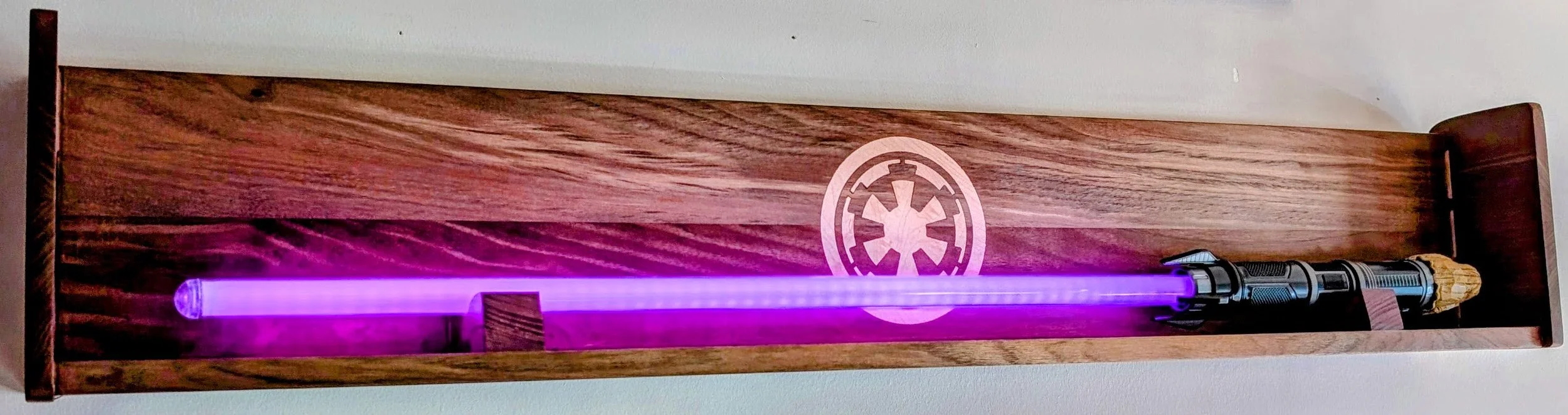 Star Wars-themed wooden display case with a purple lightsaber prop and a small Star Wars figurine, mounted on a wall with a Star Wars Imperial emblem.