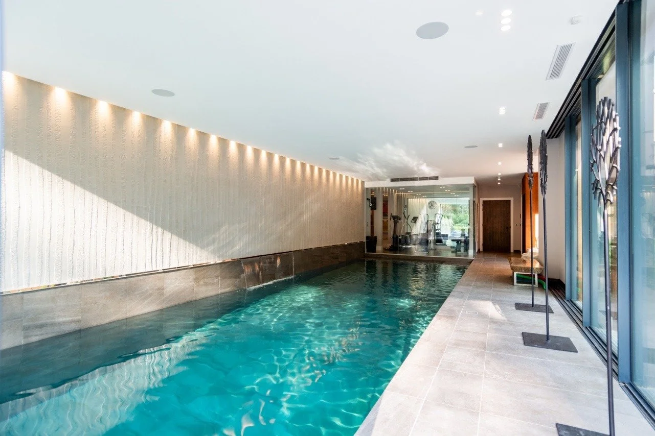 Indoor swimming pool with sunlight, modern decor, yoga mats, and exercise equipment visible through a glass wall.