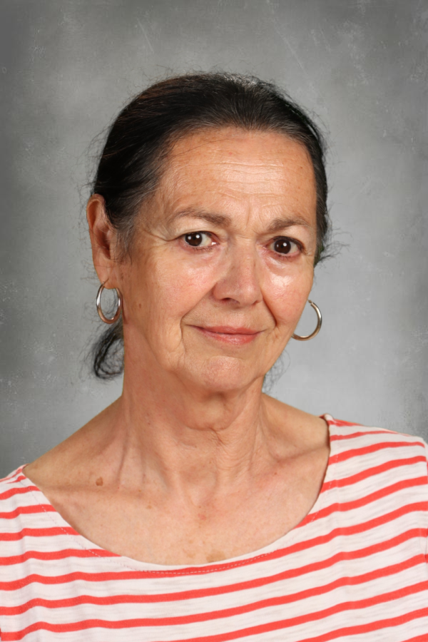 A woman with dark hair in a ponytail, wearing hoop earrings and a red and white striped shirt, smiling with a neutral gray background.