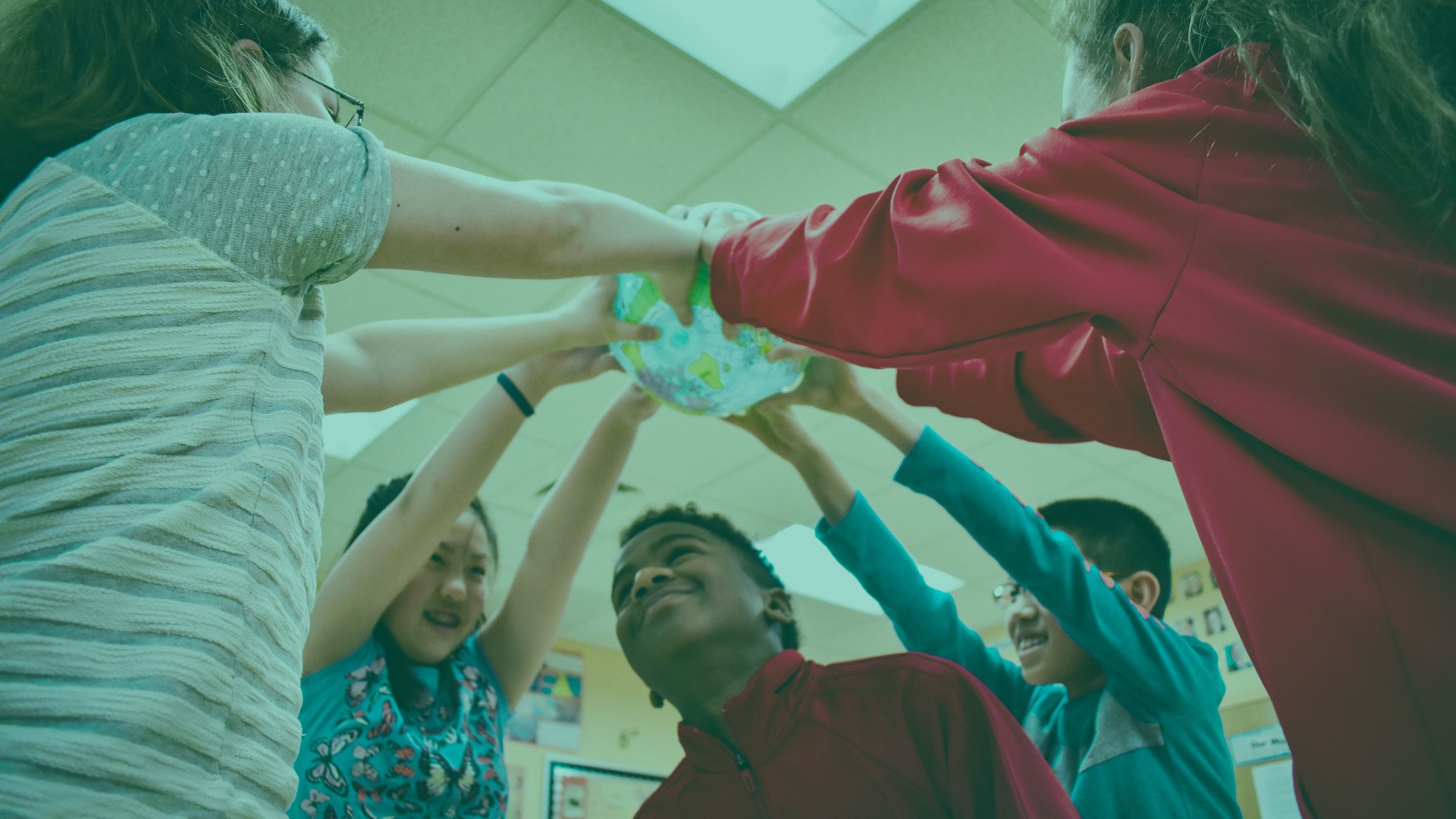 Children participating in a classroom activity, holding a globe together in a circle.