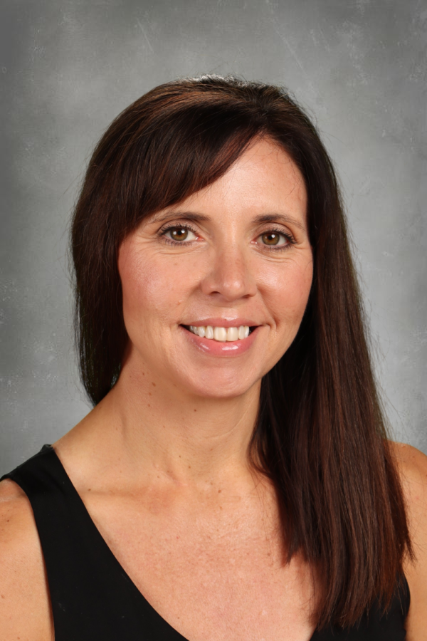 A smiling woman with straight dark brown hair and light brown eyes, wearing a black sleeveless top, standing against a gray textured background.