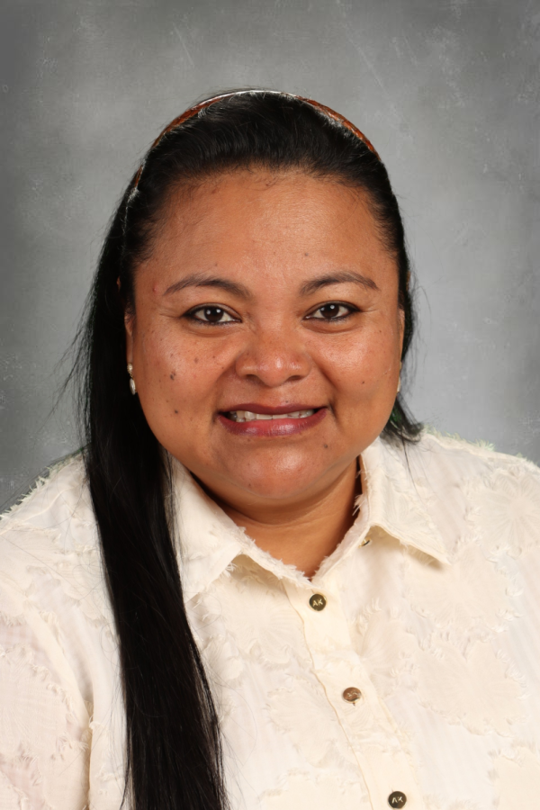 A woman with long black hair wearing a white blouse with gold buttons and pearl earrings, smiling against a gray background.