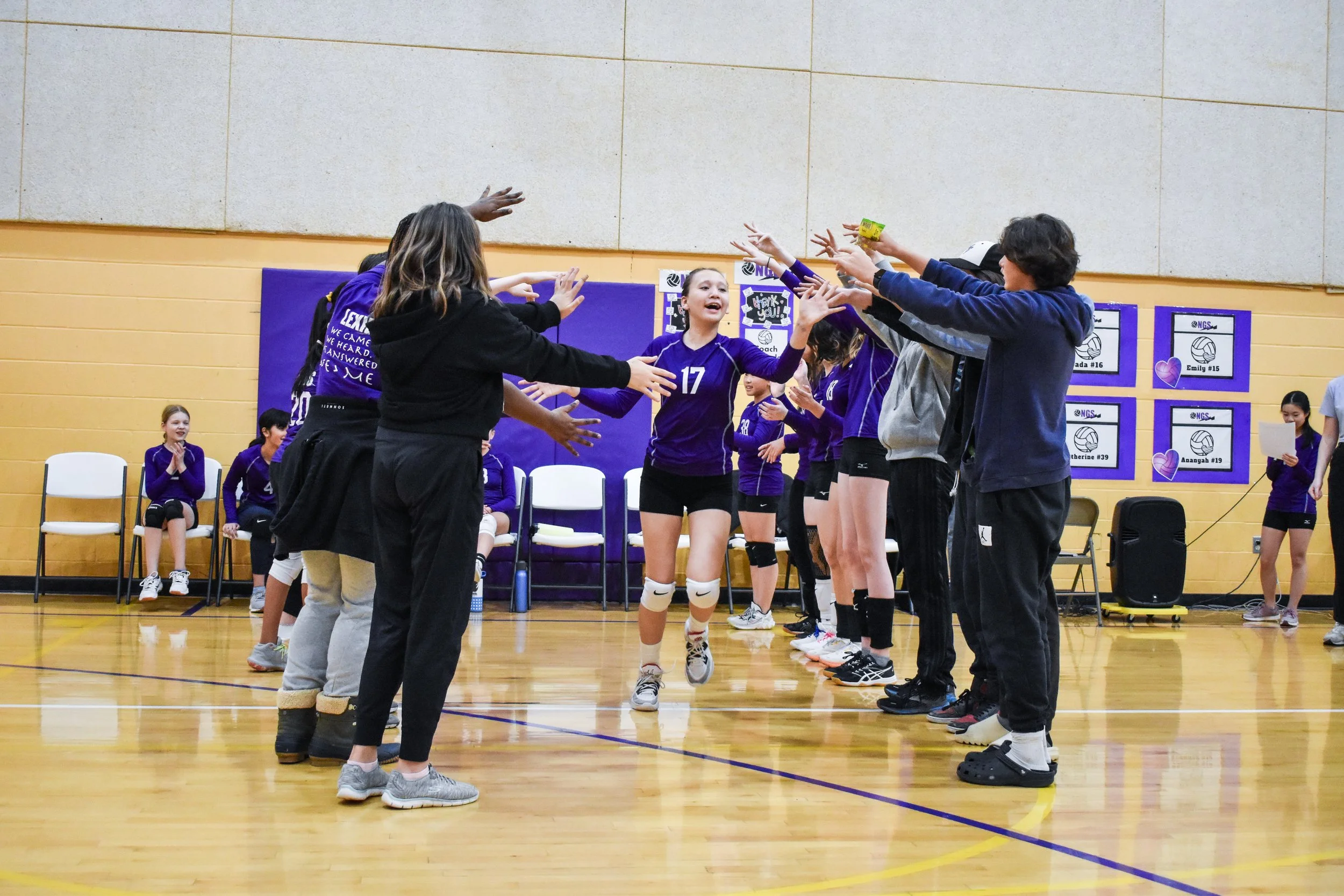 Girls volleyball team celebrating with high fives during a game in a gymnasium.