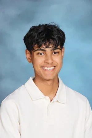 Young man with dark curly hair, wearing a white polo shirt, smiling against a blue background.