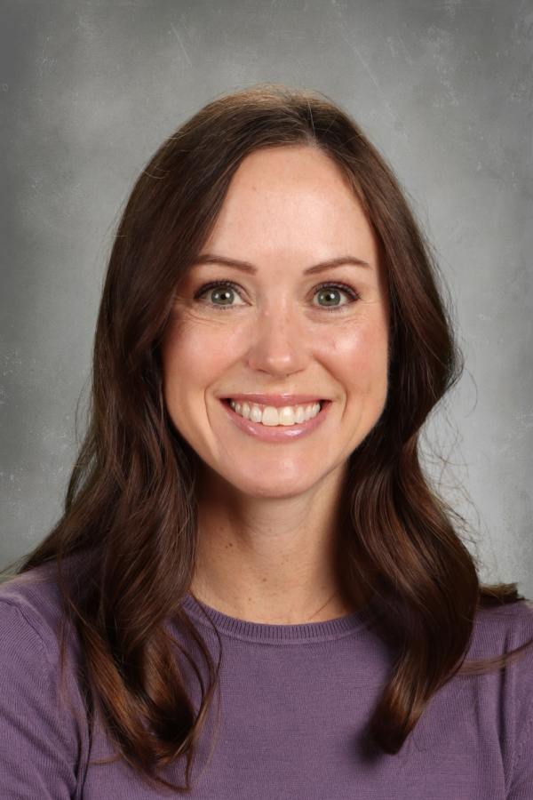 A woman with long brown hair and a purple shirt smiling against a neutral background.