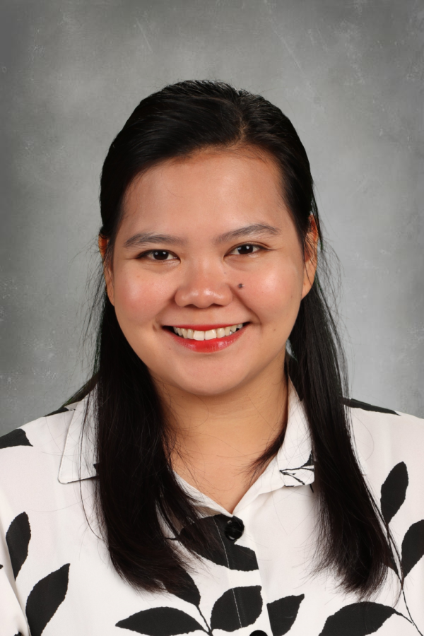 A woman with long black hair smiling, wearing a white shirt with black leaf patterns, against a gray background.