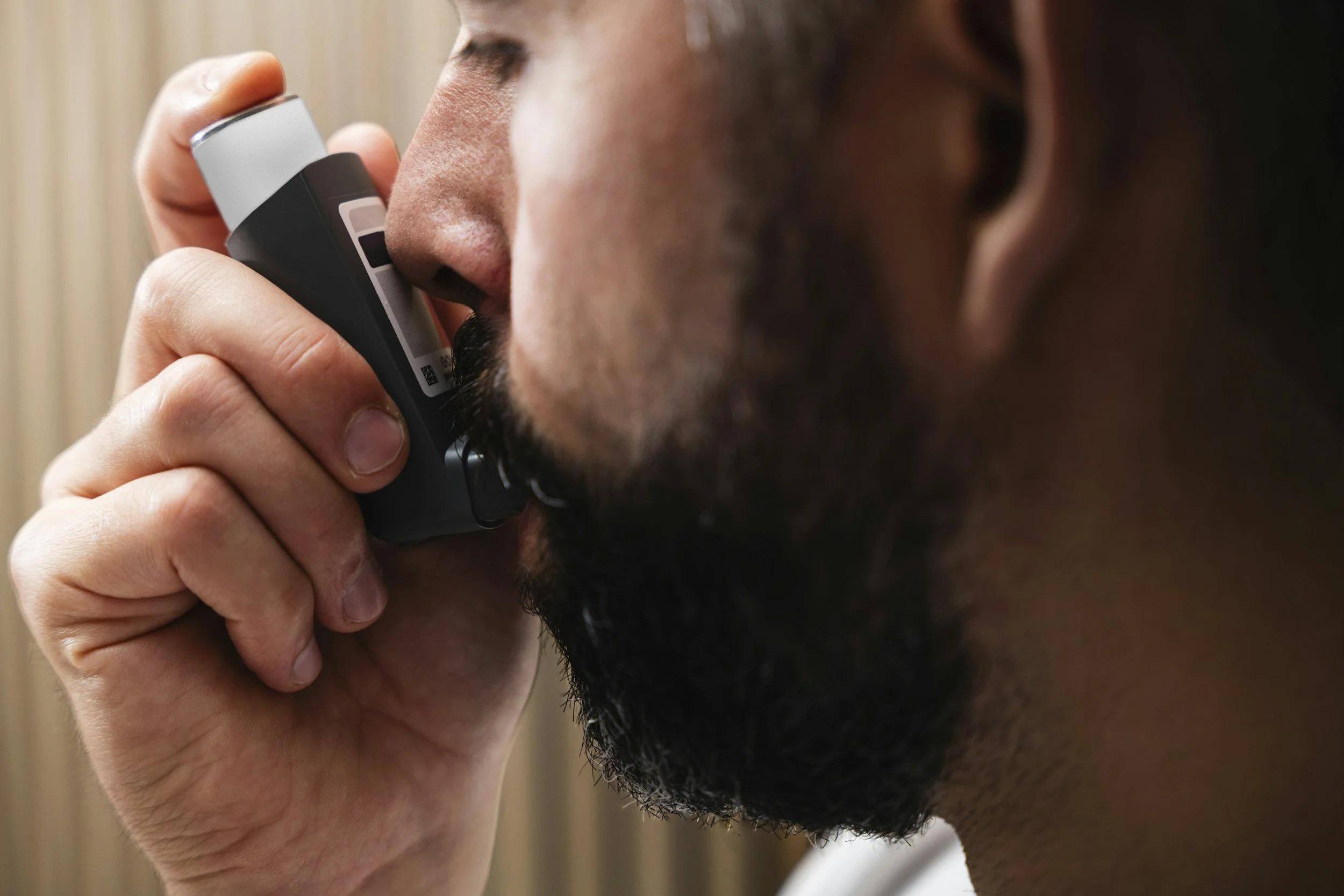 A man with a beard holds an asthma inhaler close to his nose, preparing to use it.
