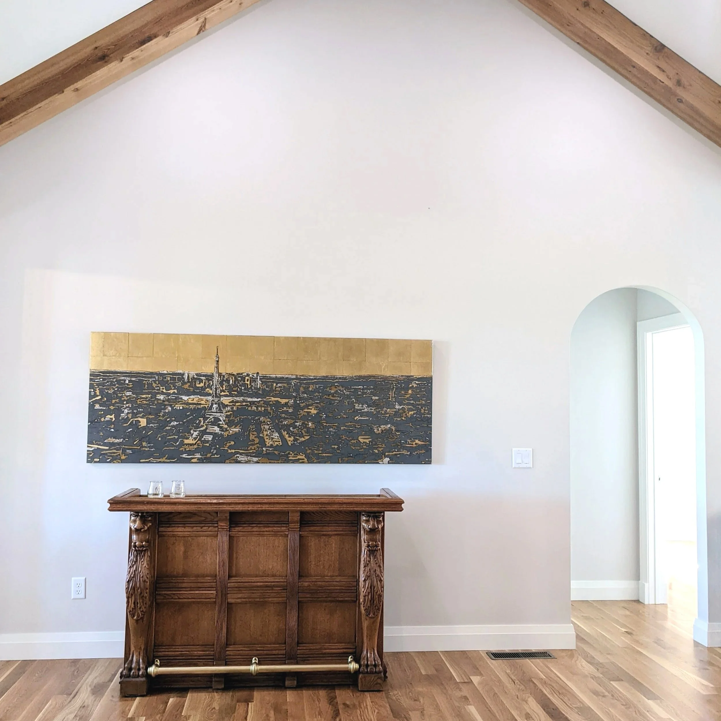 Living room with an antique art deco bar, a Paris cityscape painting with a gold background, and an arched doorway.
