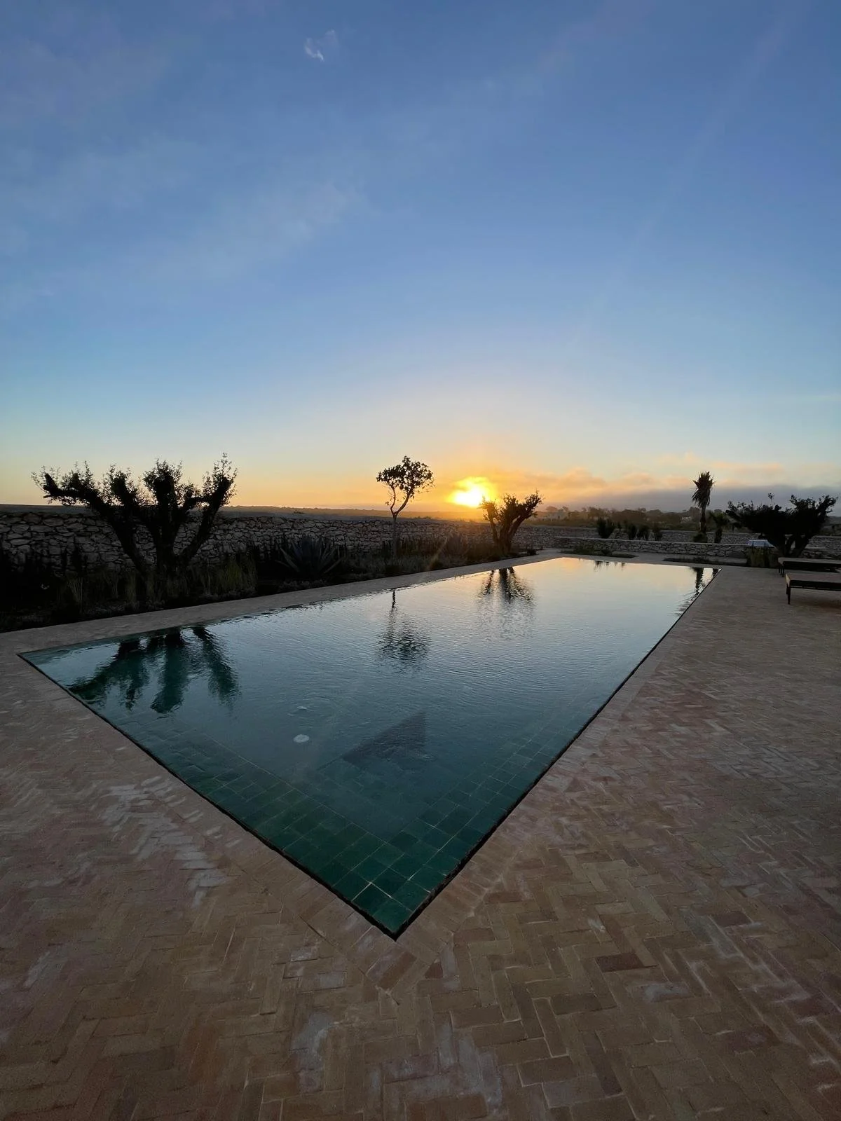 Une piscine au coucher du soleil, avec des arbres en arrière-plan et un ciel clair.
