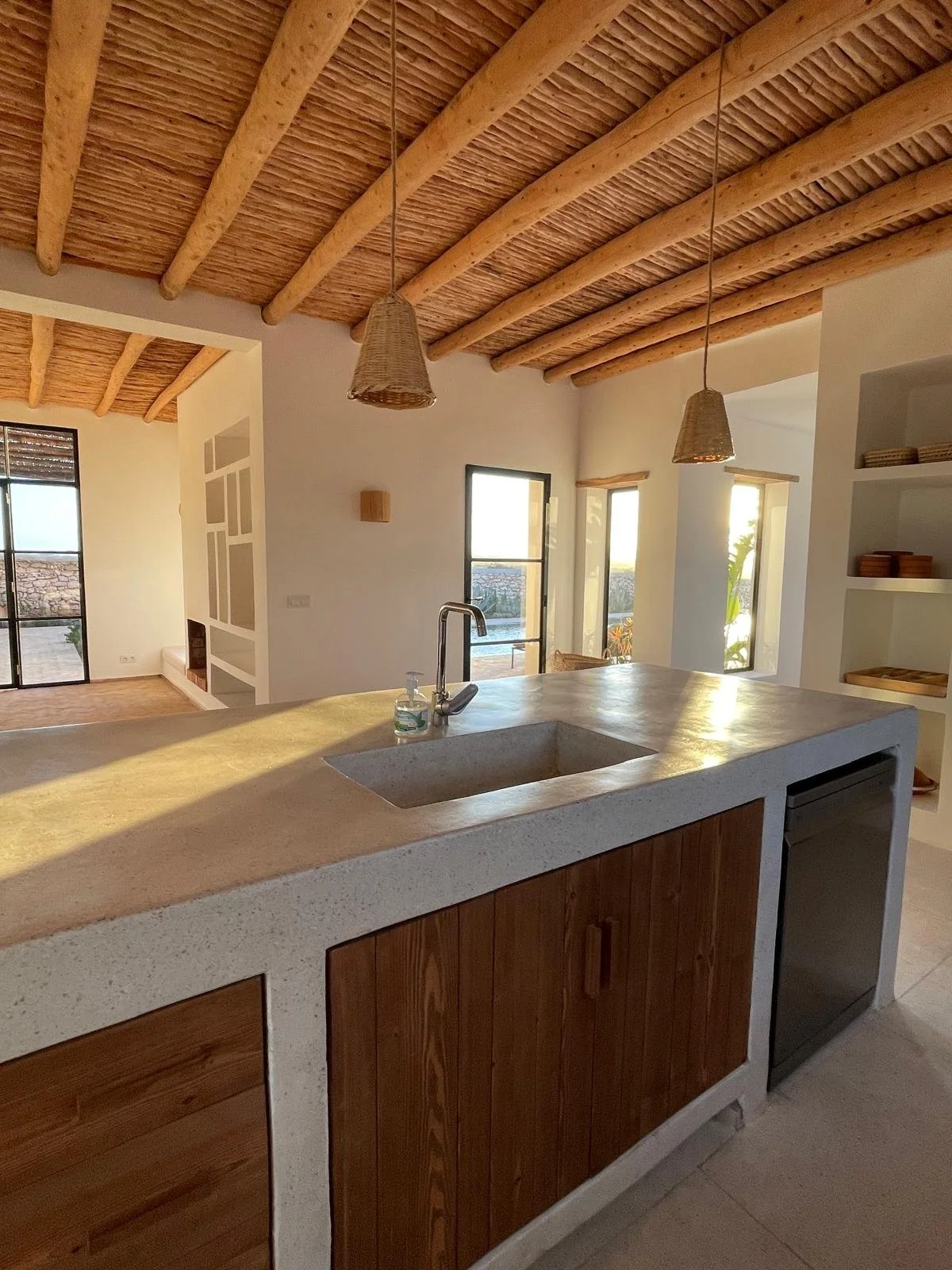Cuisine avec un plan de travail en béton, évier, robinet, armoires en bois, lumière naturelle, à l'intérieur, style moderne, avec des lampes suspendues en rotin