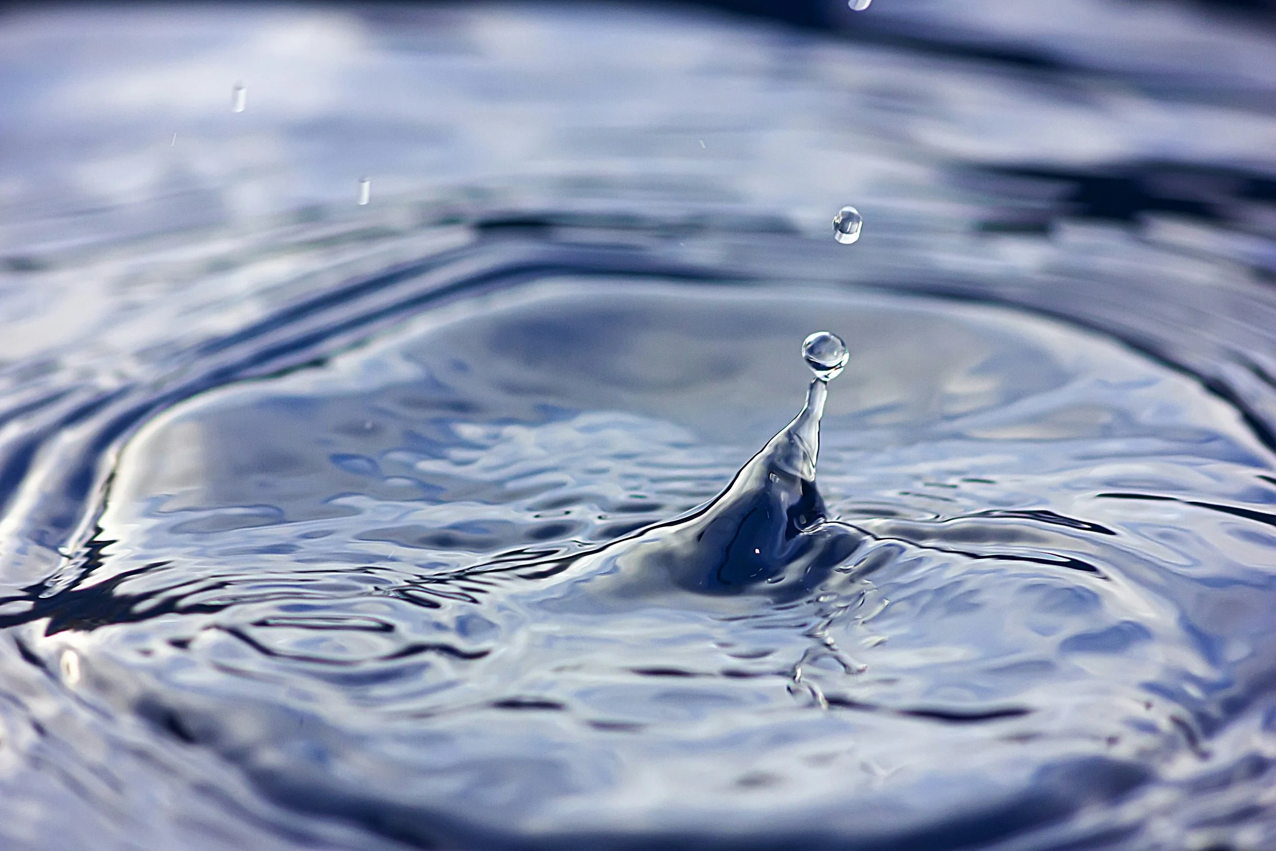 Close-up of a water droplet splashing and forming a column on the surface of blue water.