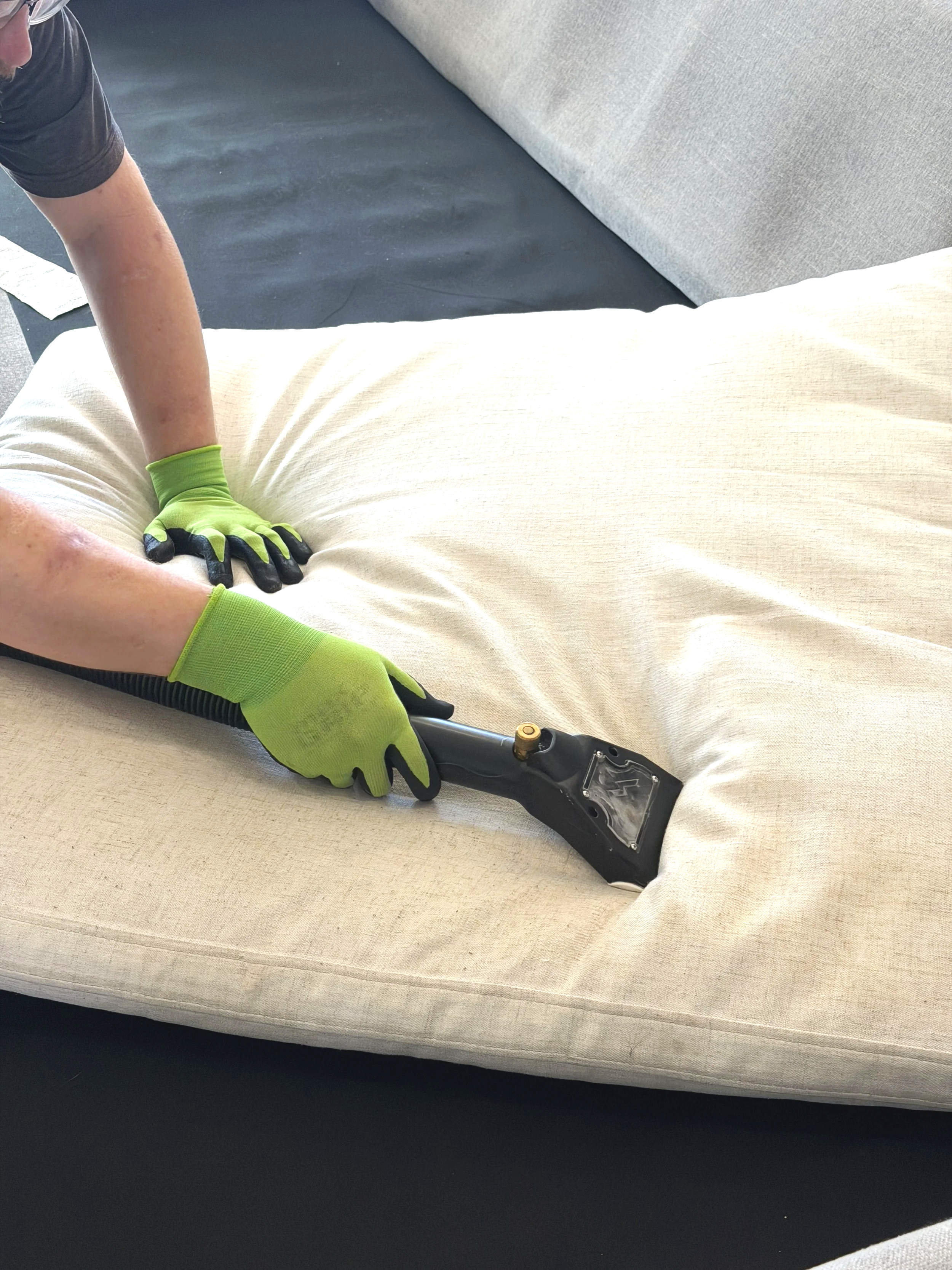 Technician professionally cleaning a couch with handheld steam cleaner