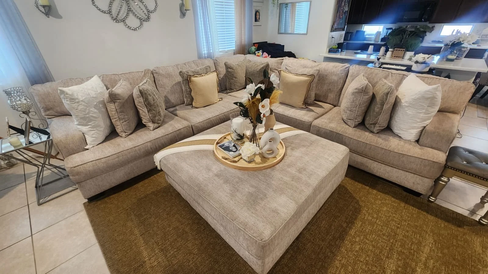 A beige sectional sofa with multiple decorative pillows, a round ottoman that were deep cleaned.