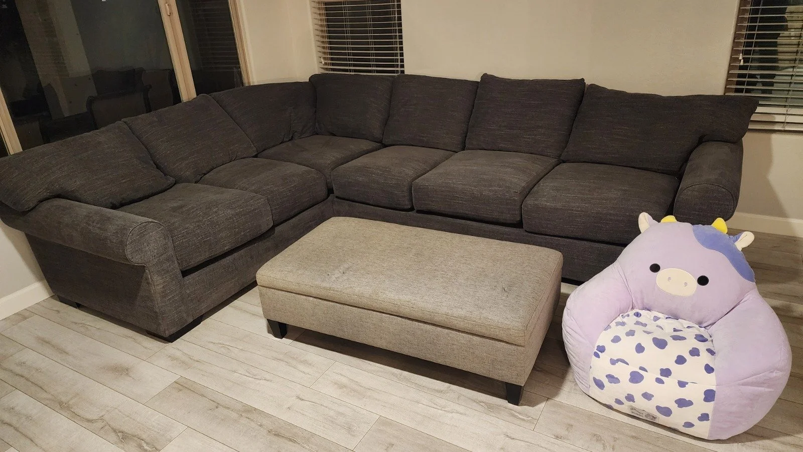 A dark gray sectional sofa with a beige ottoman in front that was professionally cleaned