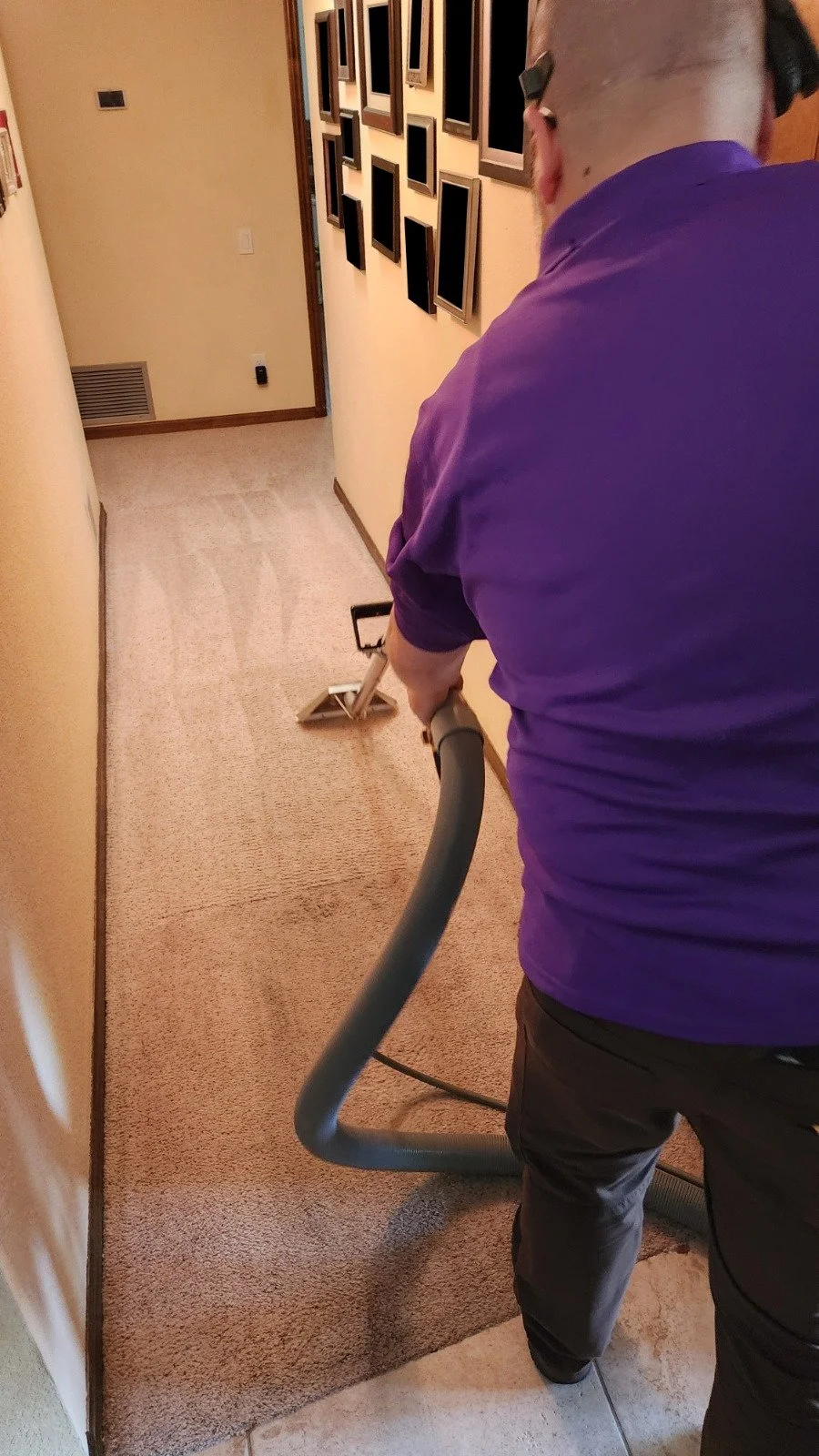 A person is steam cleaning a beige carpet in a narrow hallway.